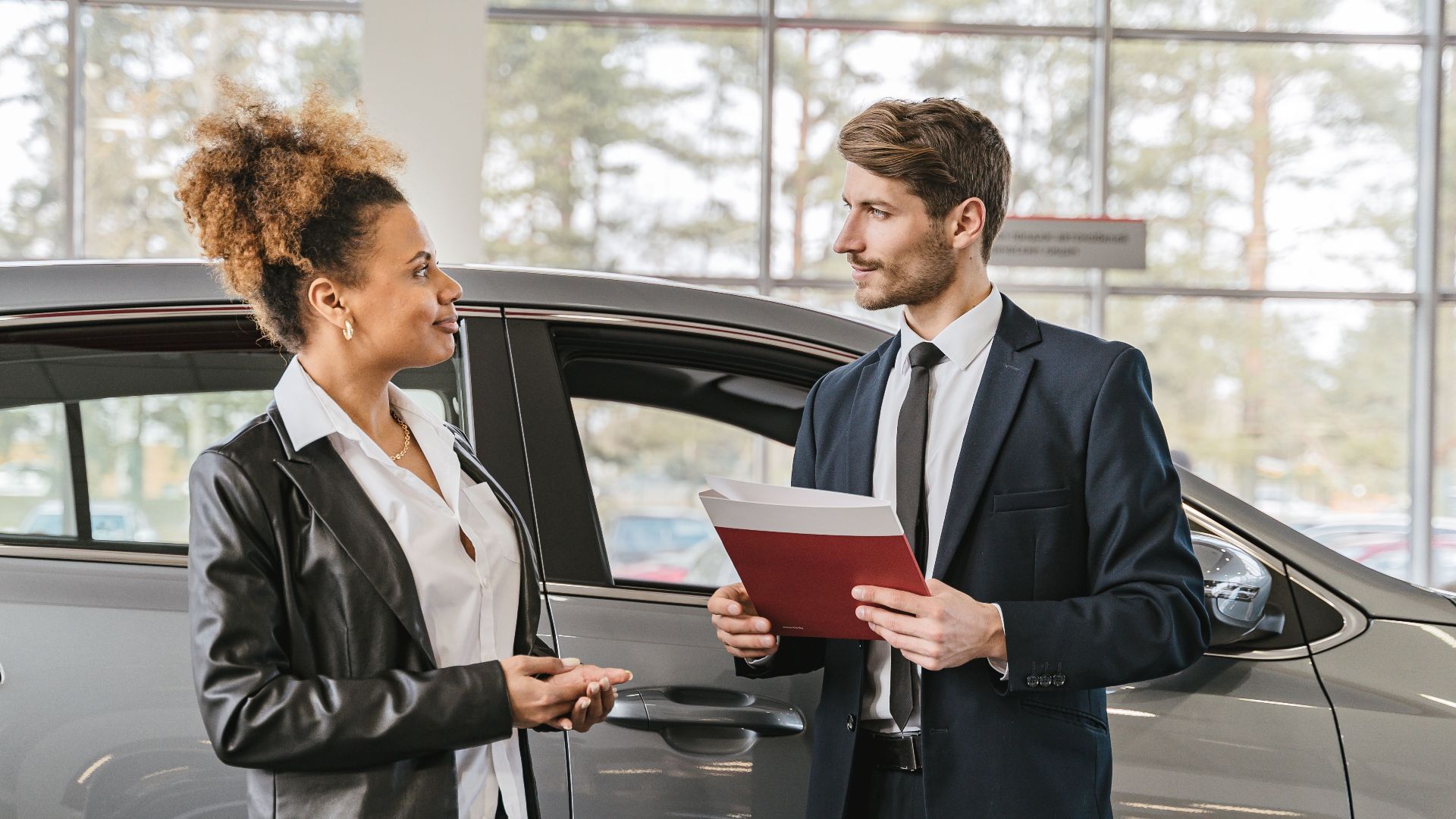 A woman discussing car purchase with a dealer inside a car dealership showroom.