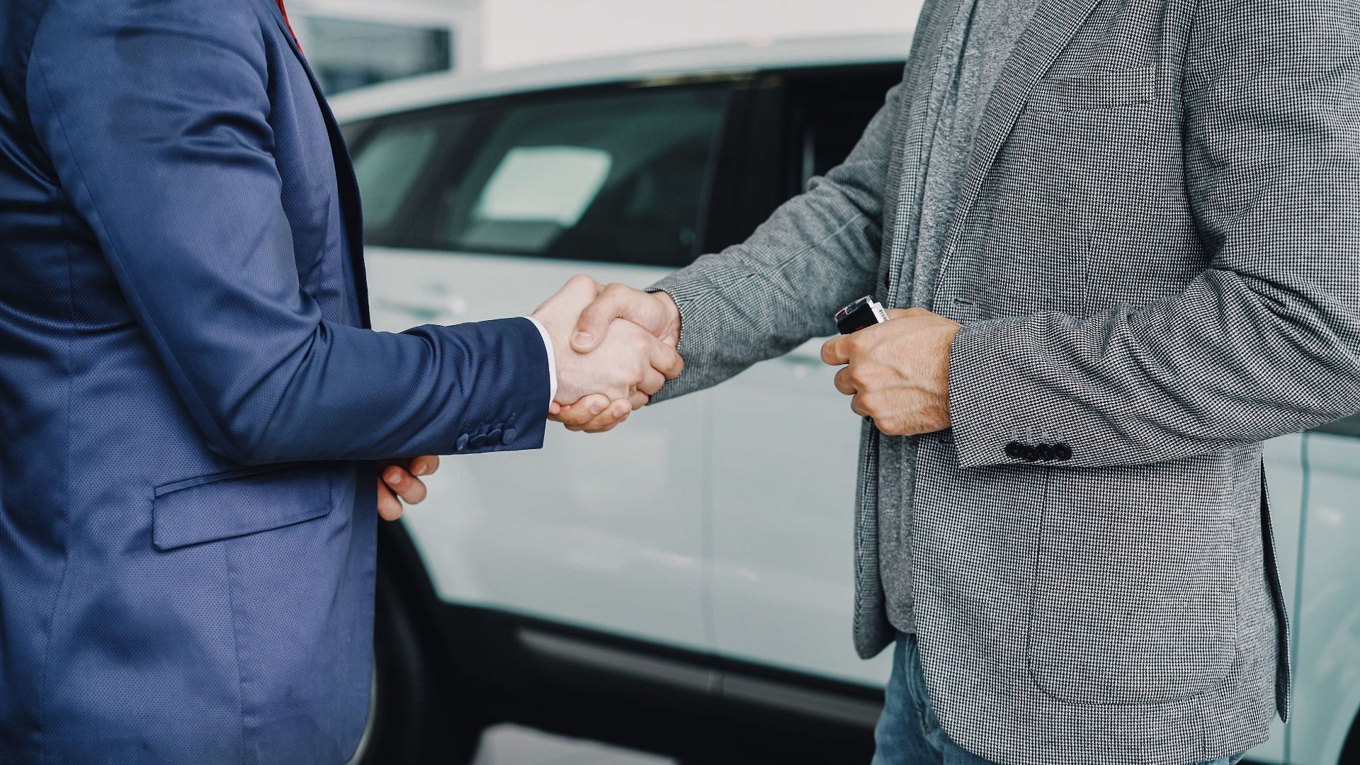 Two businessmen shaking hands in a car dealership, sealing a deal.