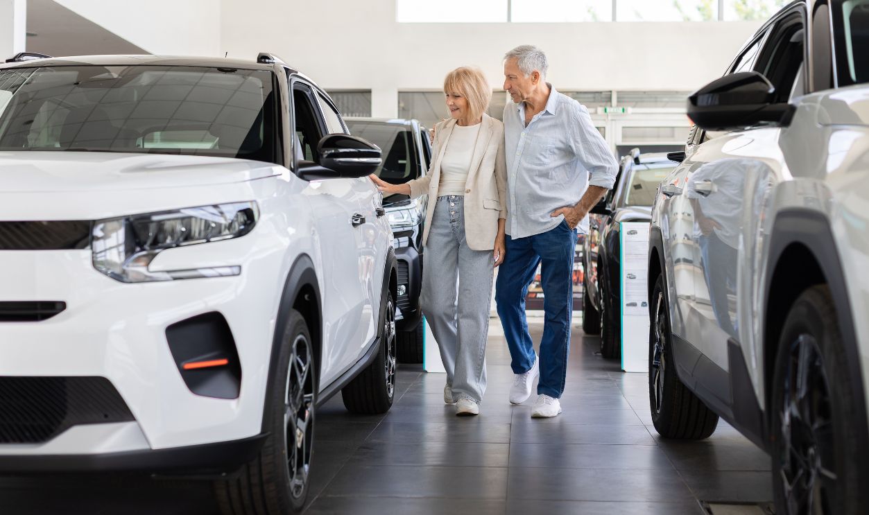 Shutterstock-2853259941, Senior Caucasian couple walks through a modern car dealership showroom, comparing displayed vehicles and discussing available options before choosing an automobile to purchase
