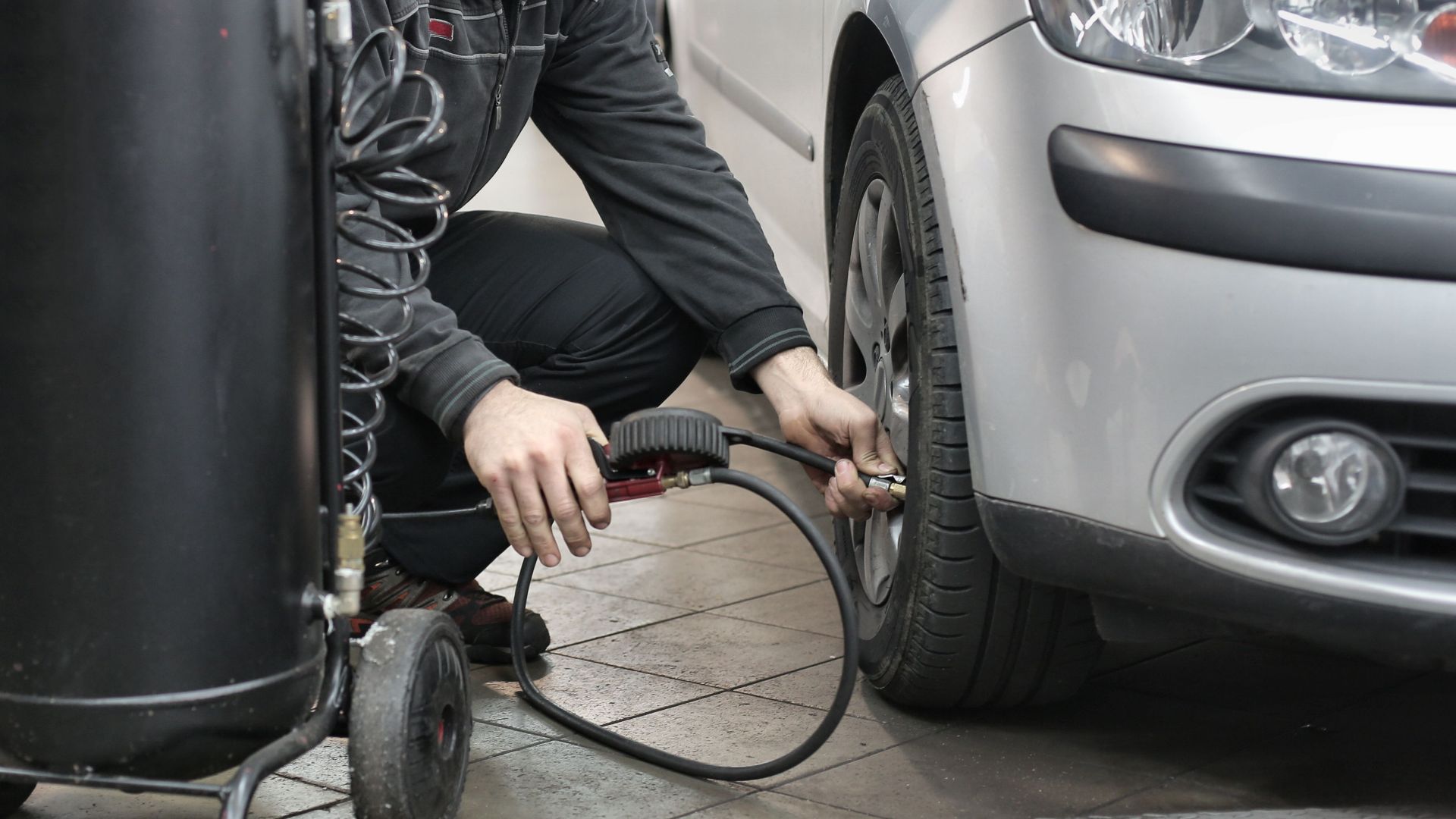 Mechanic inspecting and adjusting tire pressure in an auto repair shop.