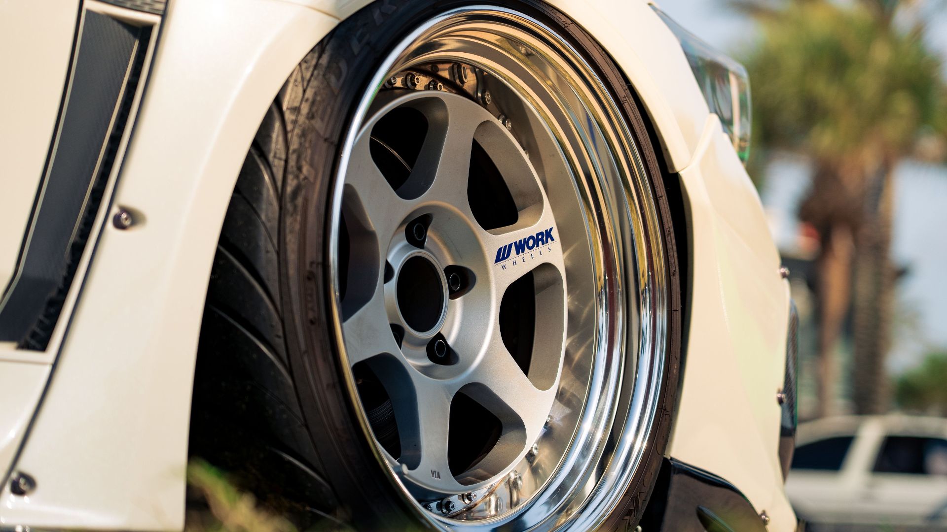 Detailed shot of a sleek car wheel featuring a chrome Work Wheels rim, outdoors.