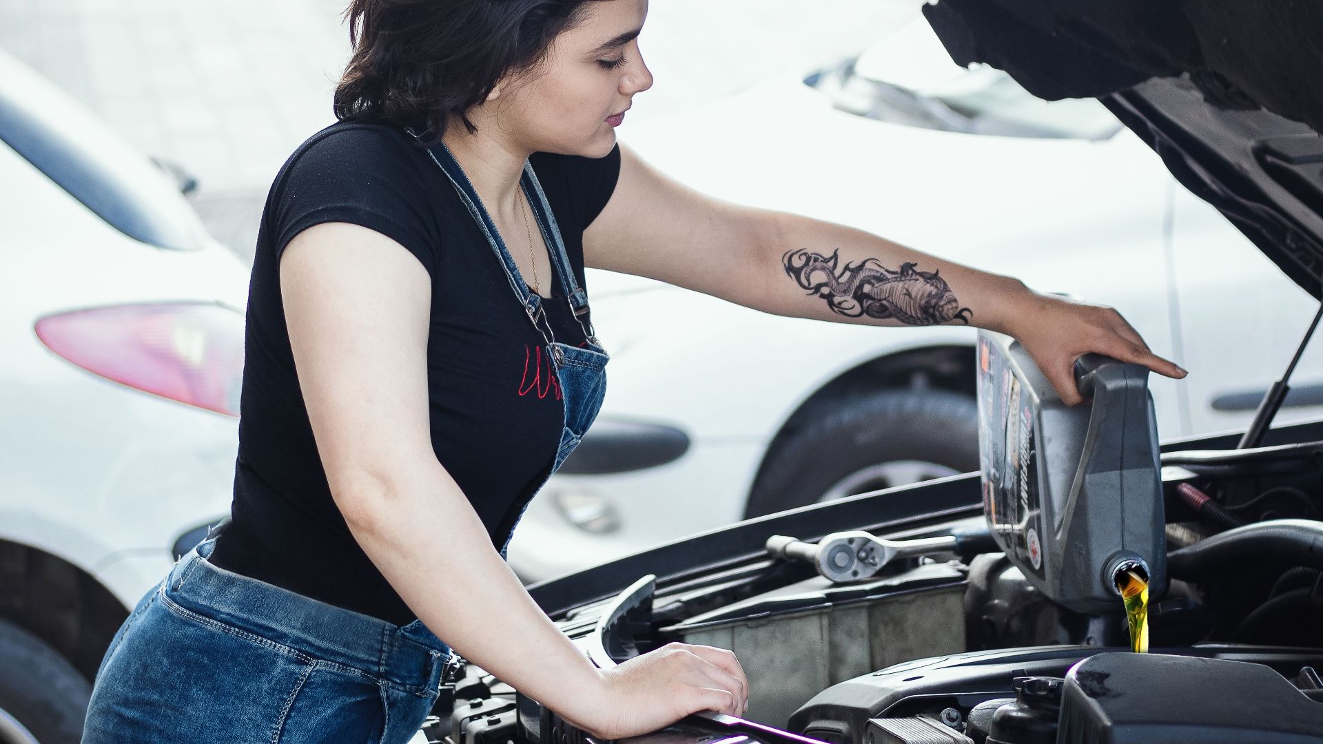 Woman adding oil to a car engine outdoors in Rasht, Iran, showcasing DIY vehicle care.