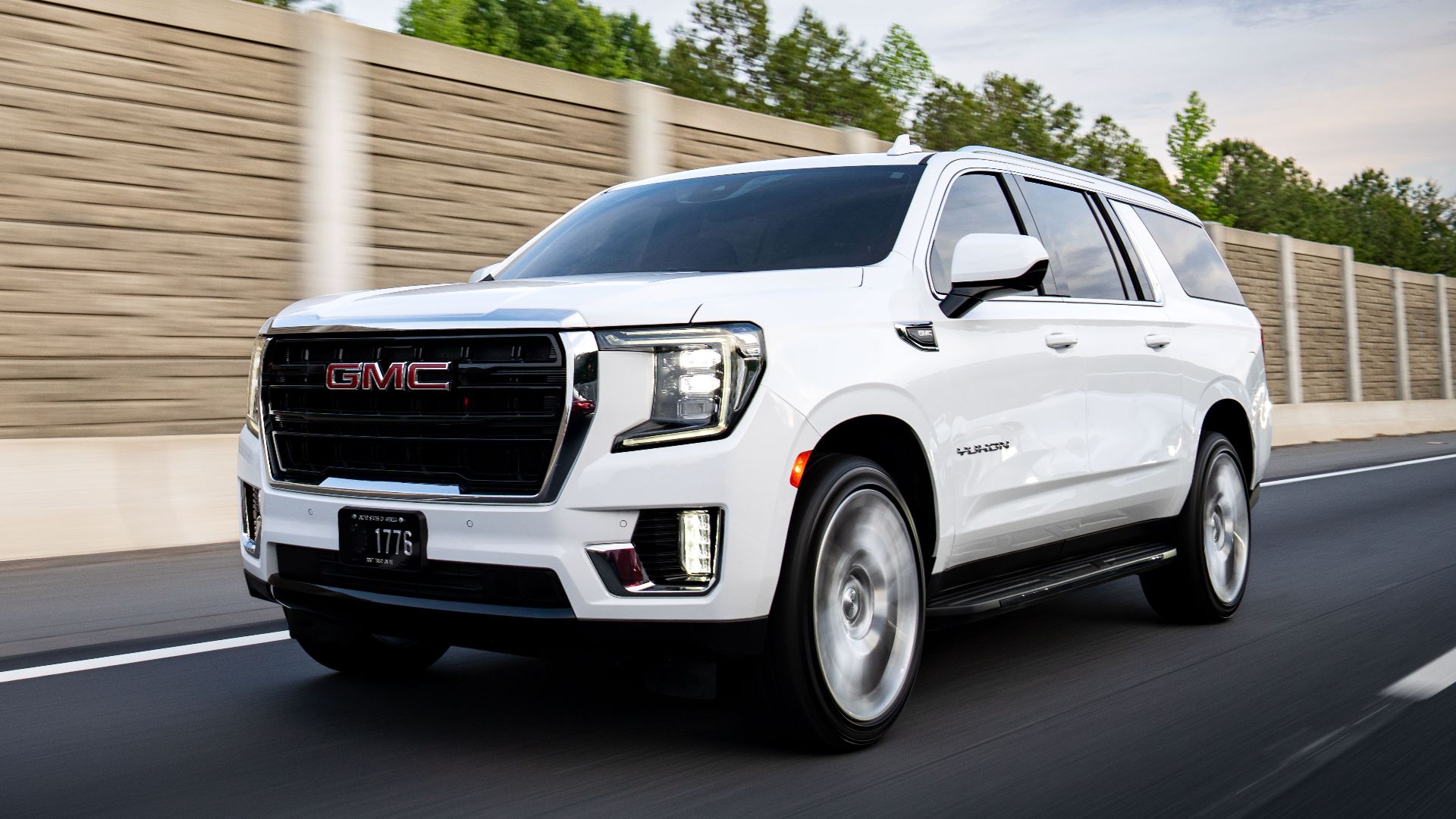White GMC Yukon XL cruising on a highway in Charlotte, North Carolina, under a clear blue sky.