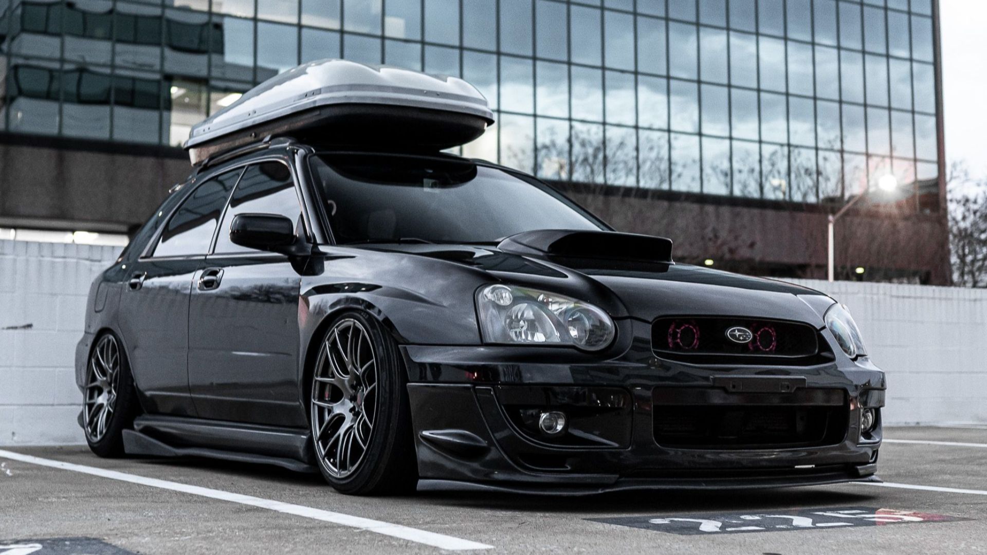 Ground level of contemporary style black racing automobile with shiny surface and luggage rack on roof parked on asphalt with marking lines near building facade in town in parking lot