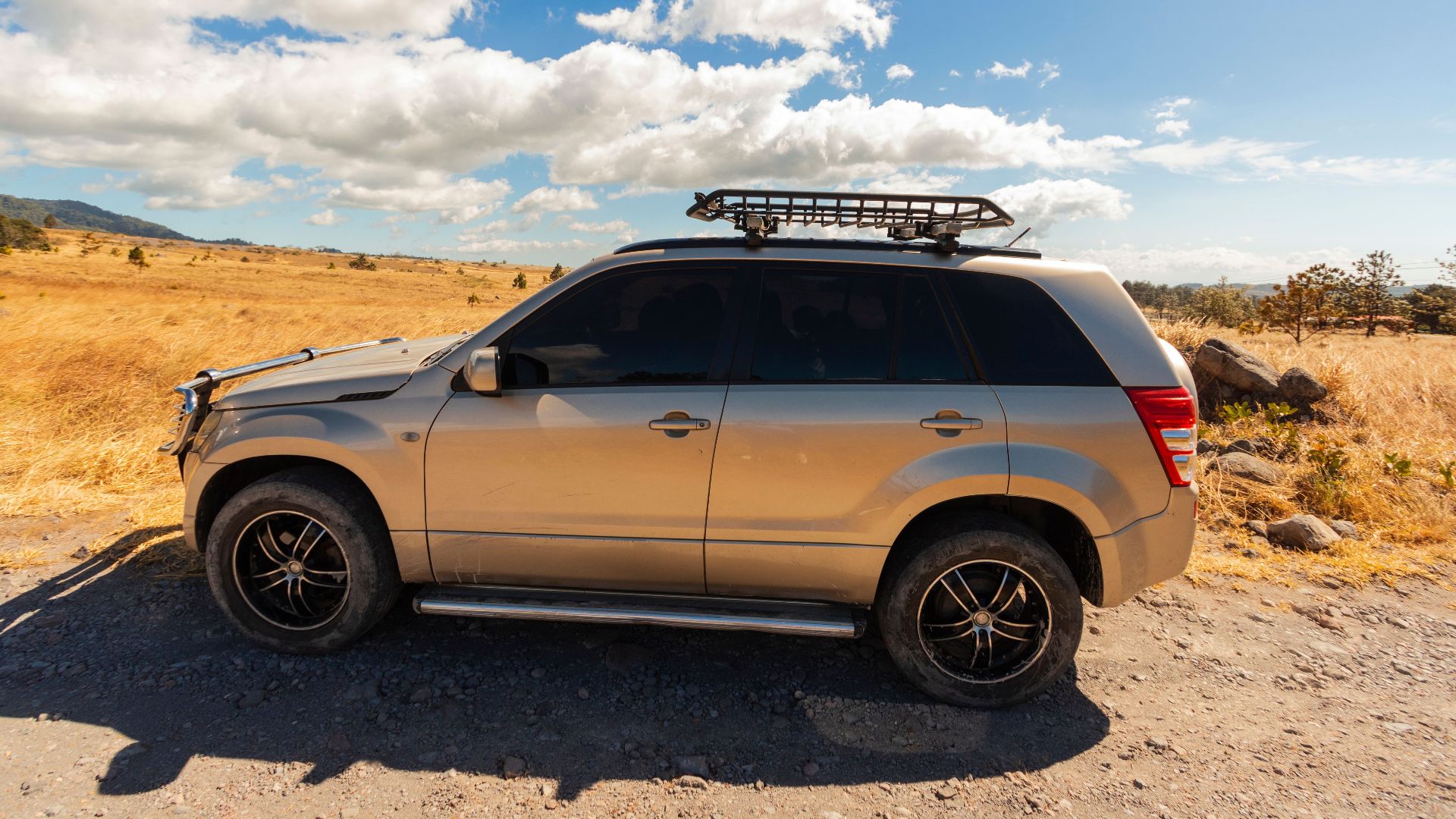 Side view of a silver SUV on a sunny day, parked in a scenic countryside under a bright blue sky.