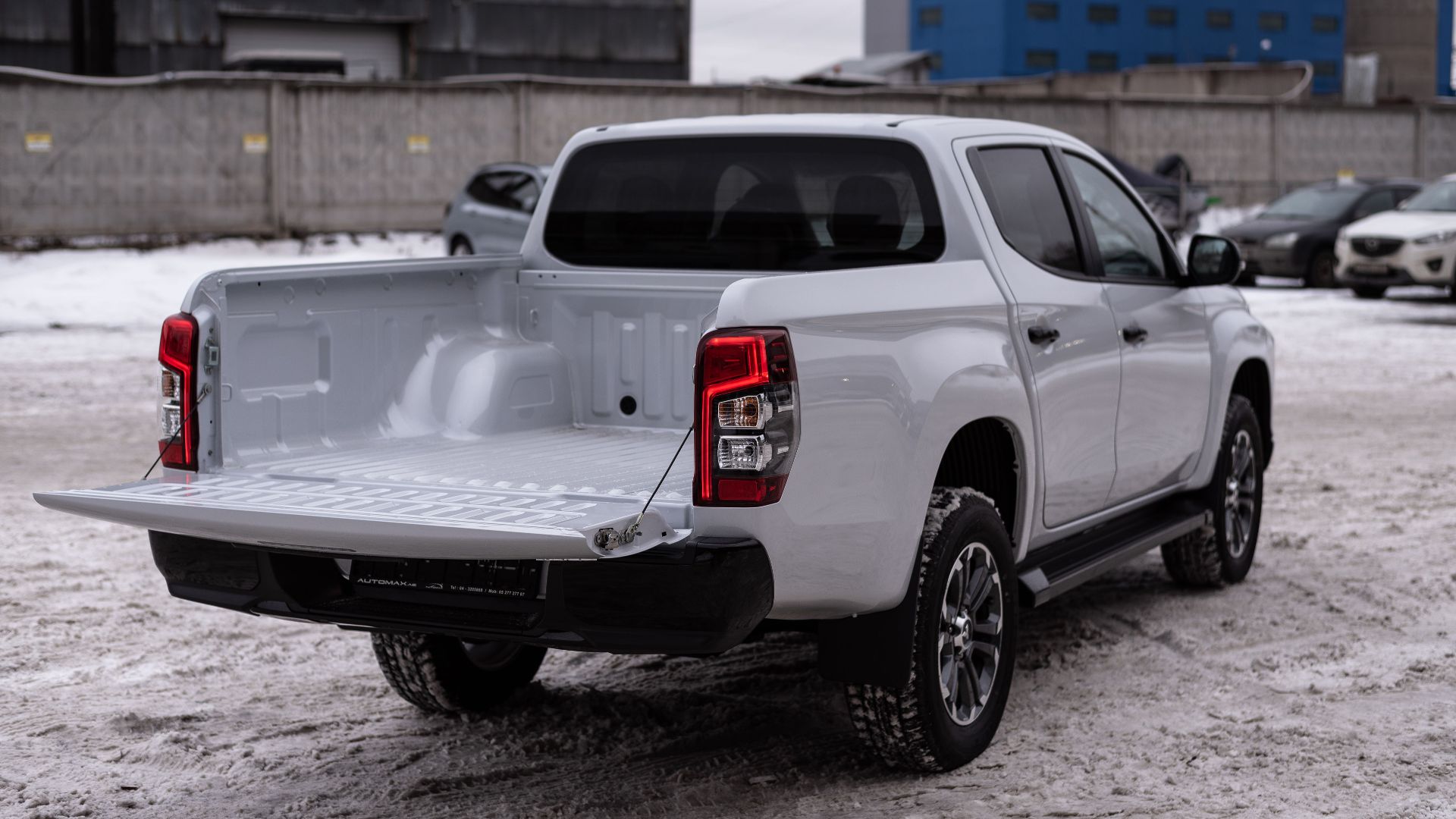 White pickup truck parked in a snowy industrial area, showcasing its open cargo bed.