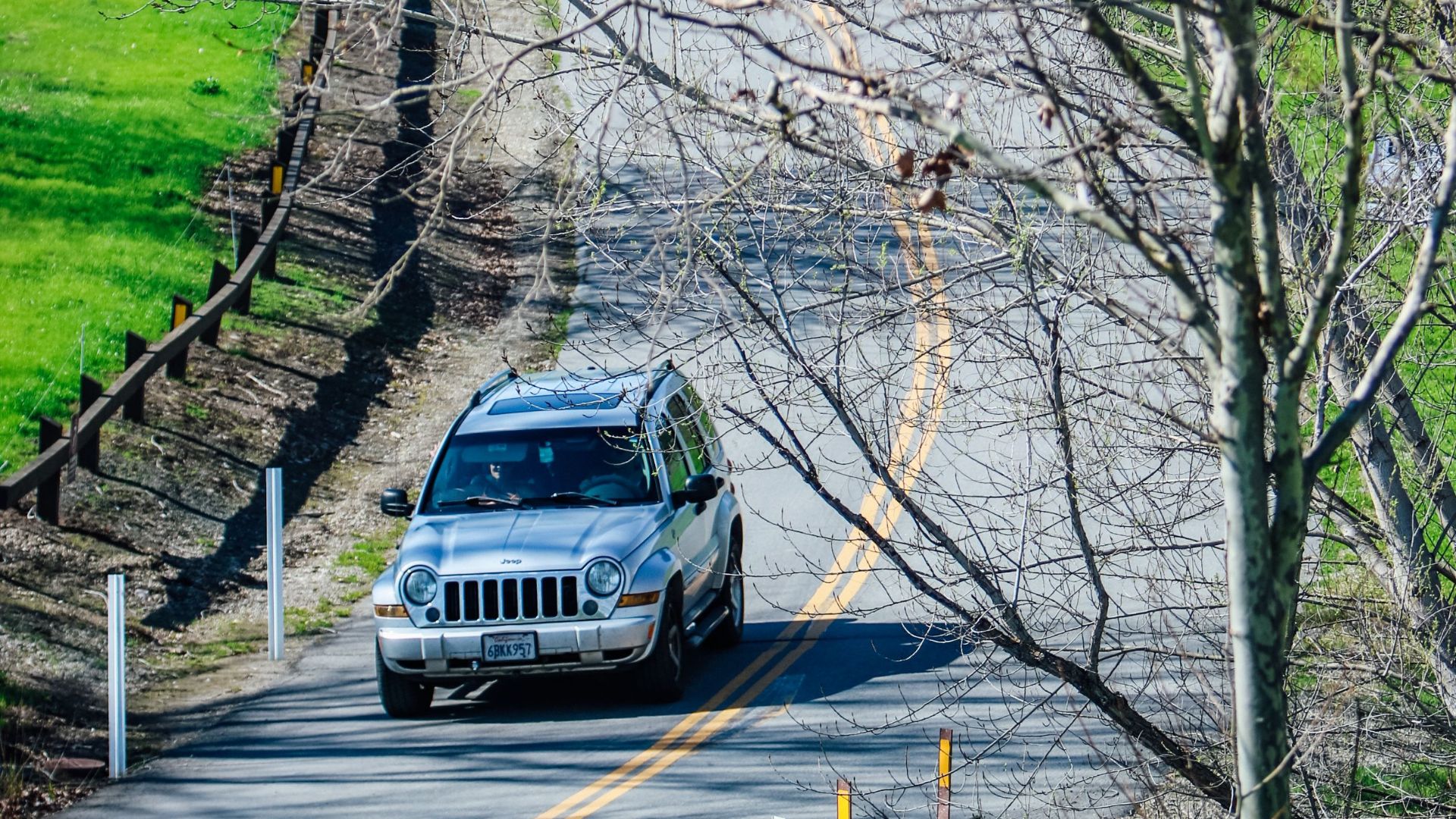 A silver SUV navigates a winding rural road surrounded by lush green countryside.