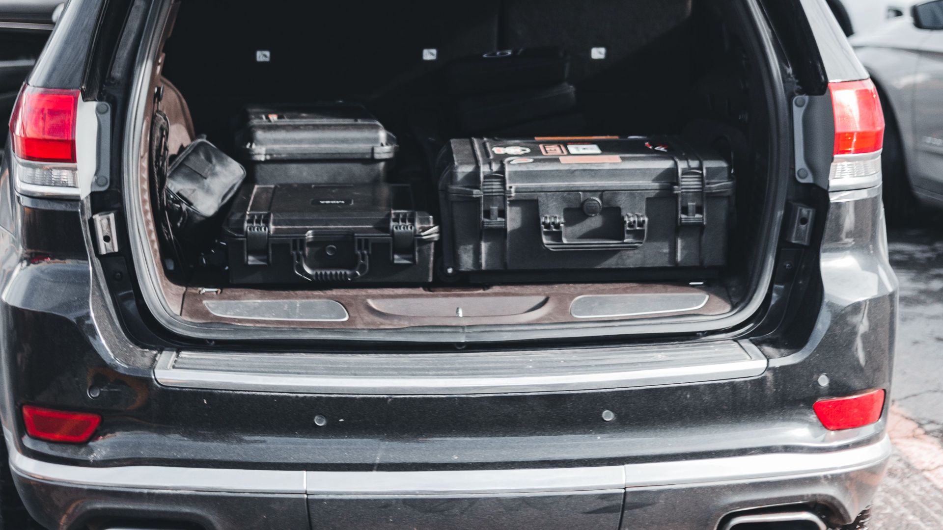 Open trunk of an SUV filled with equipment cases, parked outdoors under a cloudy sky.
