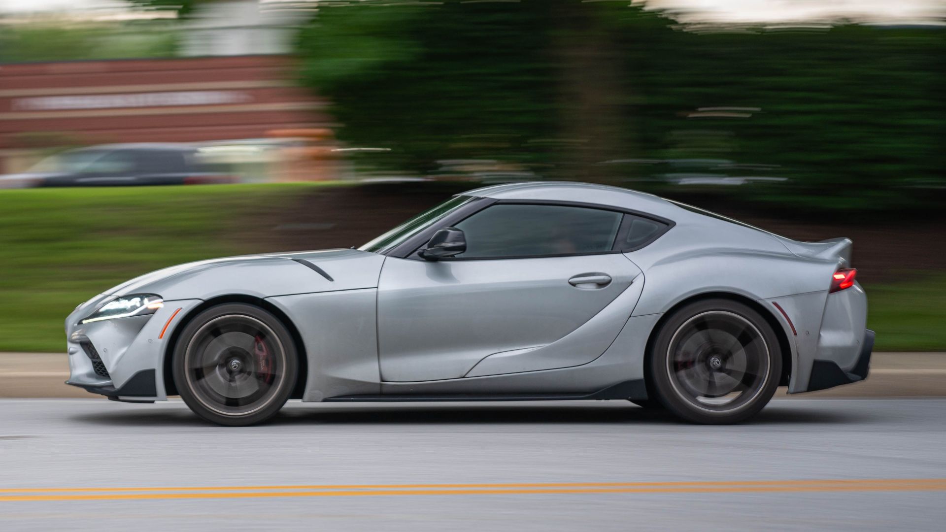 Side view of a fast silver sports car in motion on an urban road.