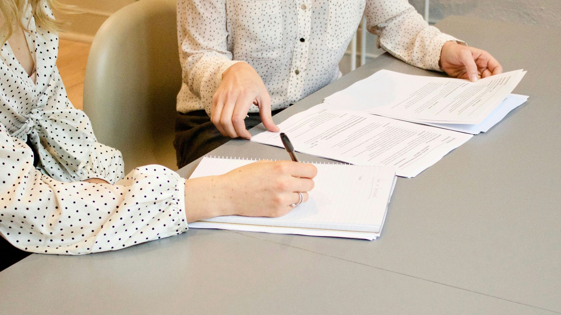 woman signing on white printer paper beside woman about to touch the documents