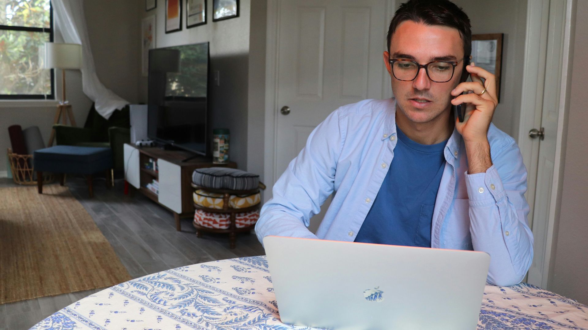man in white dress shirt wearing eyeglasses sitting by the table using macbook