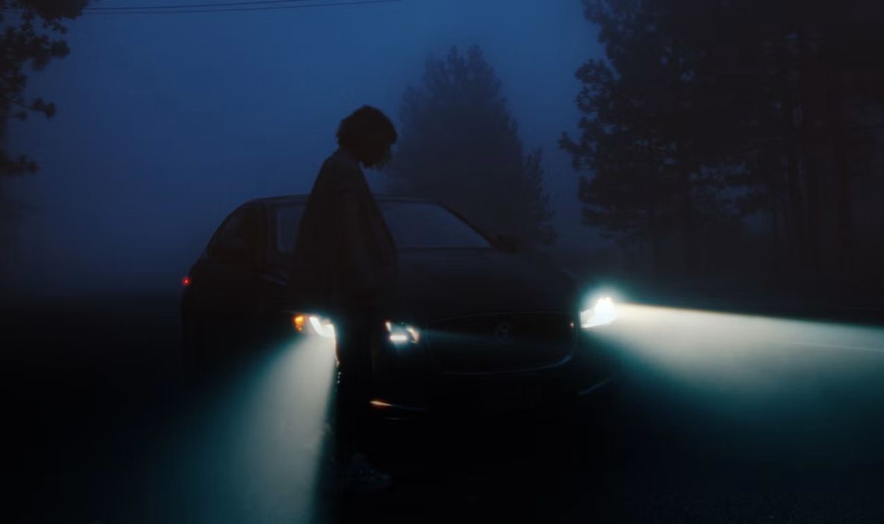 Person standing by car with headlights on at night