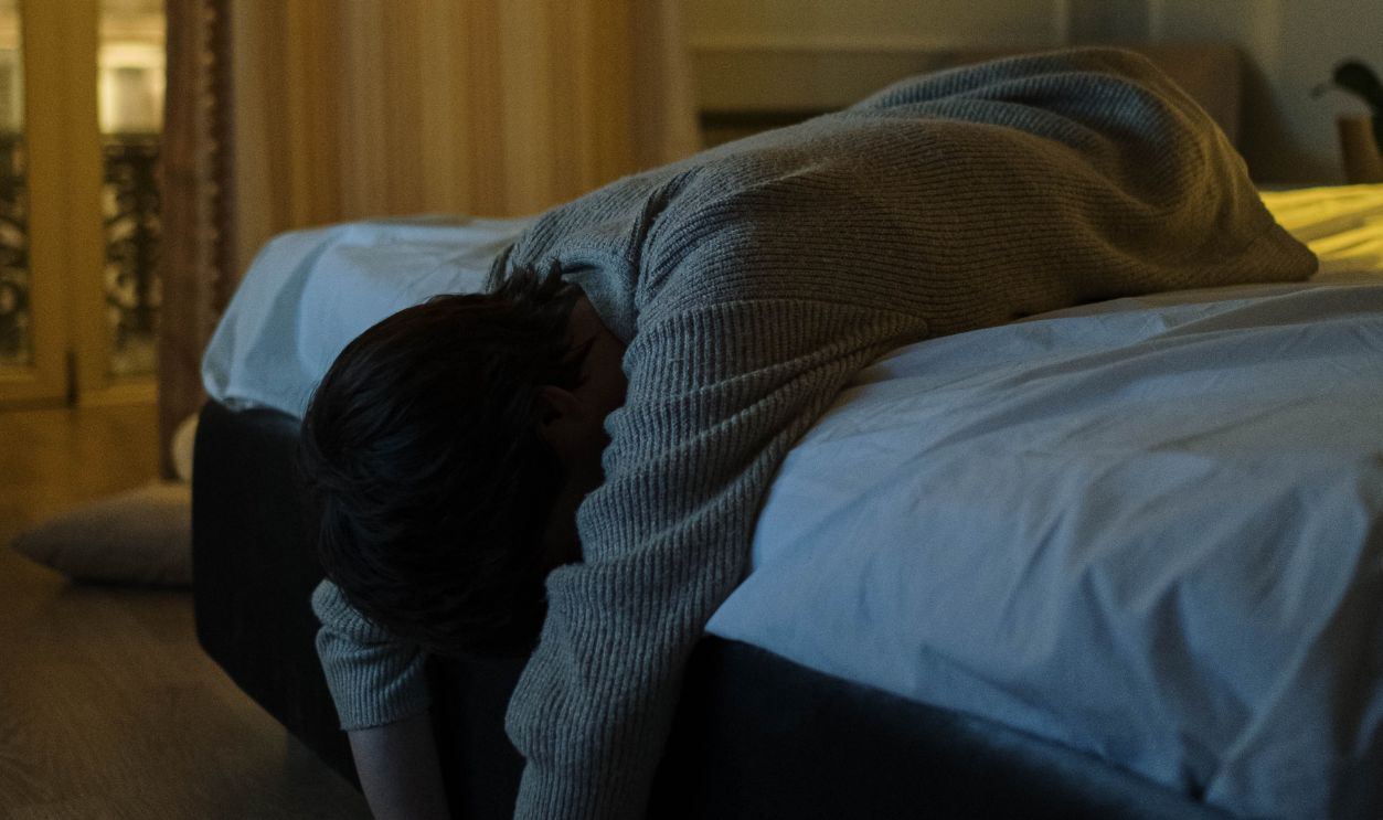 A person with gray long sleeves lying tiredly on a bed at night, feeling exhaustion and insomnia.