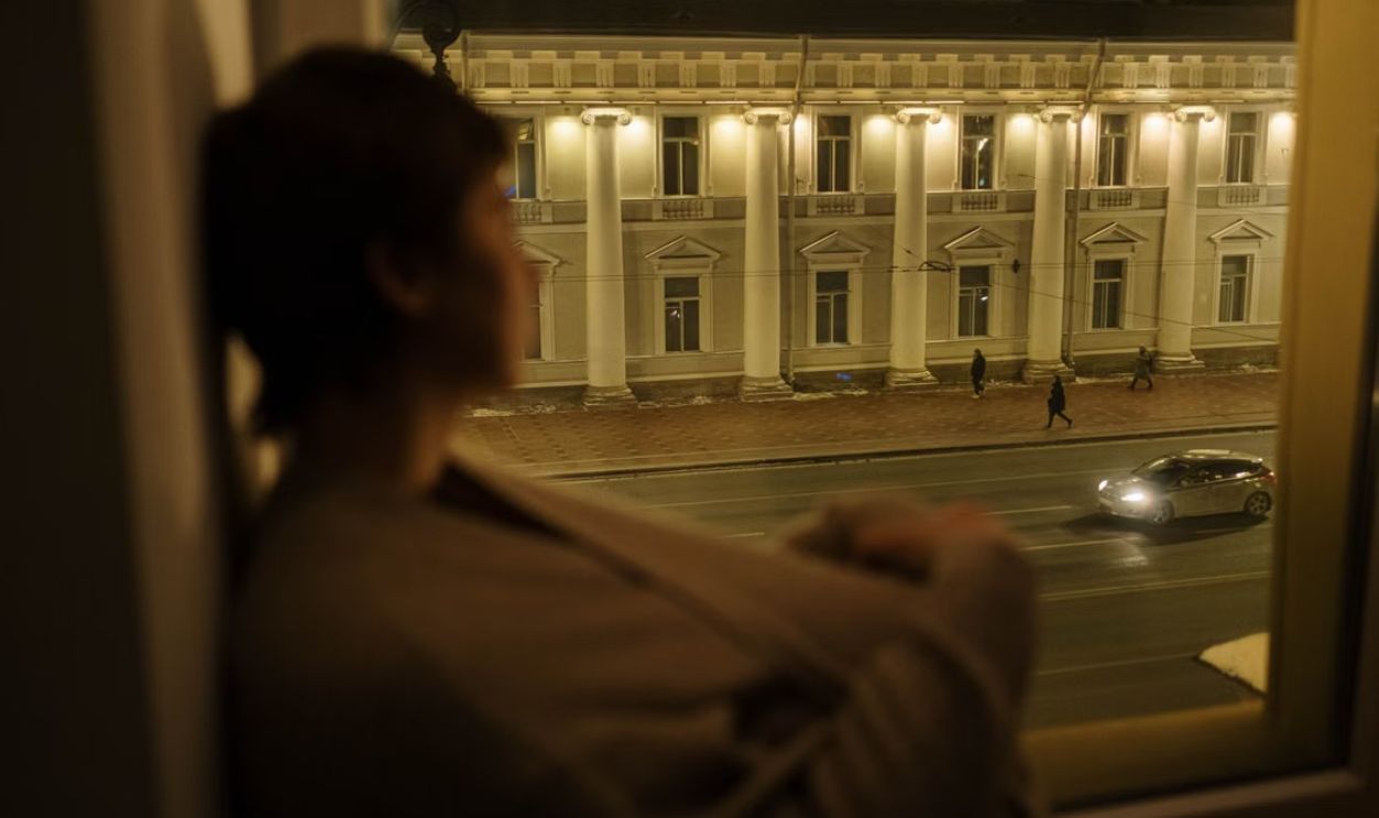 Woman gazing out a window at a city street at night, creating a serene, introspective mood.