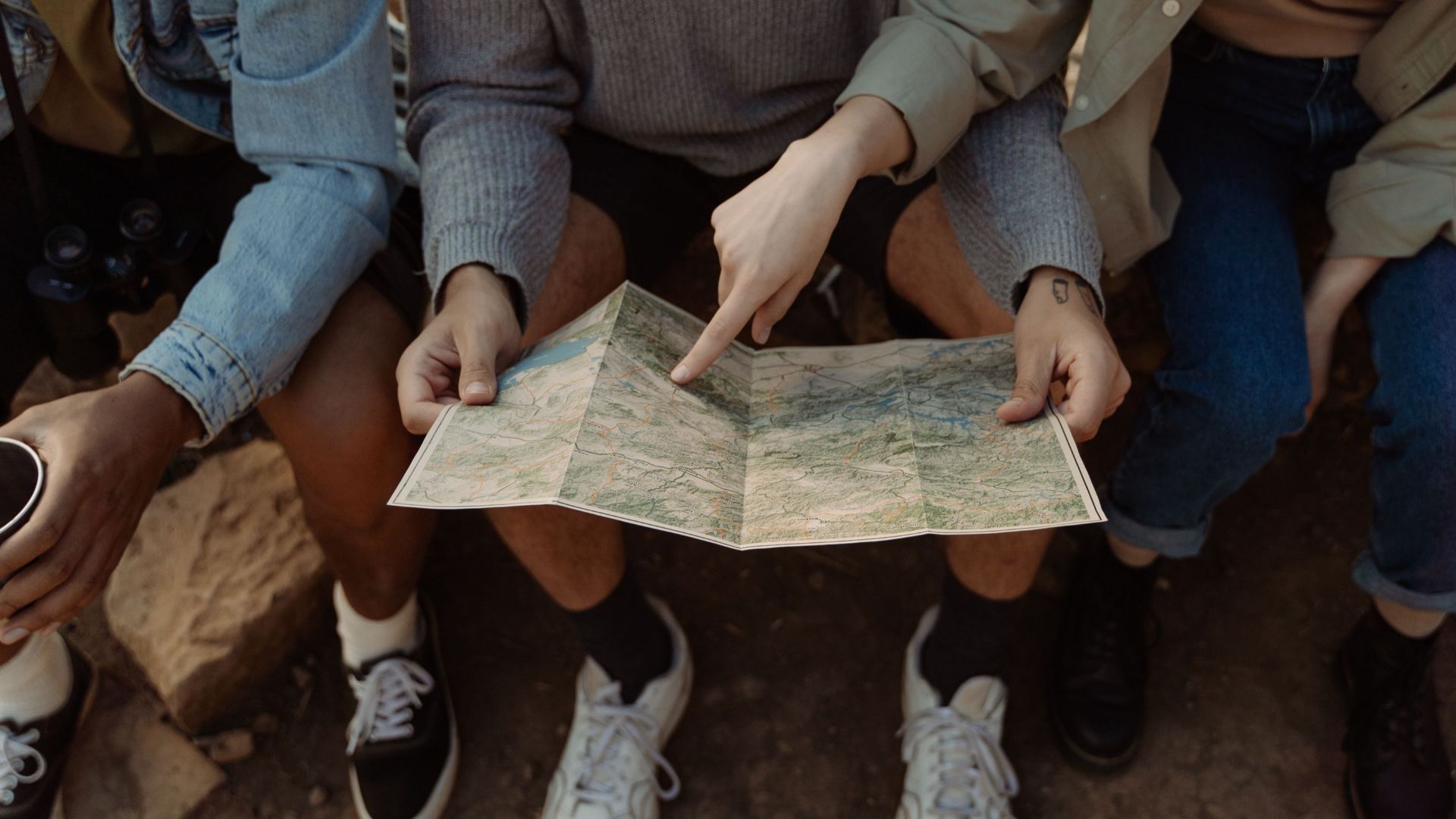 Group of friends sitting together, exploring a map for their next adventure, creating exciting travel plans.