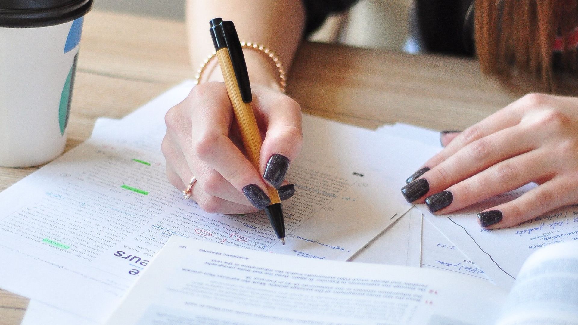 A young woman studying with a pen and coffee cup, focusing on her notes.