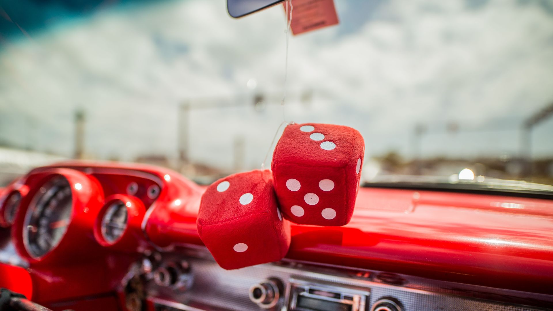 Close-up of a classic car interior with red dice hanging from the mirror, showcasing retro style.