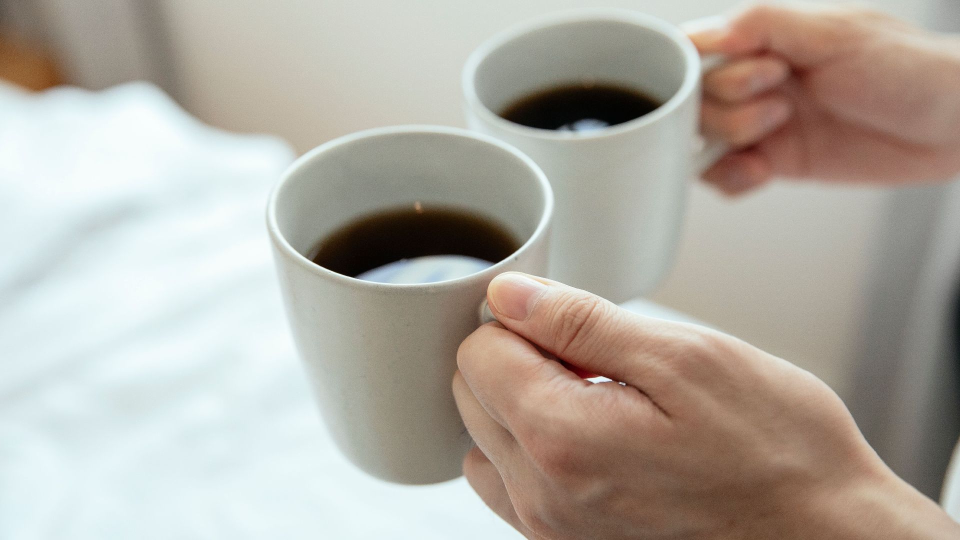 Close-up of hands holding two mugs filled with hot black coffee, perfect for a cozy morning.