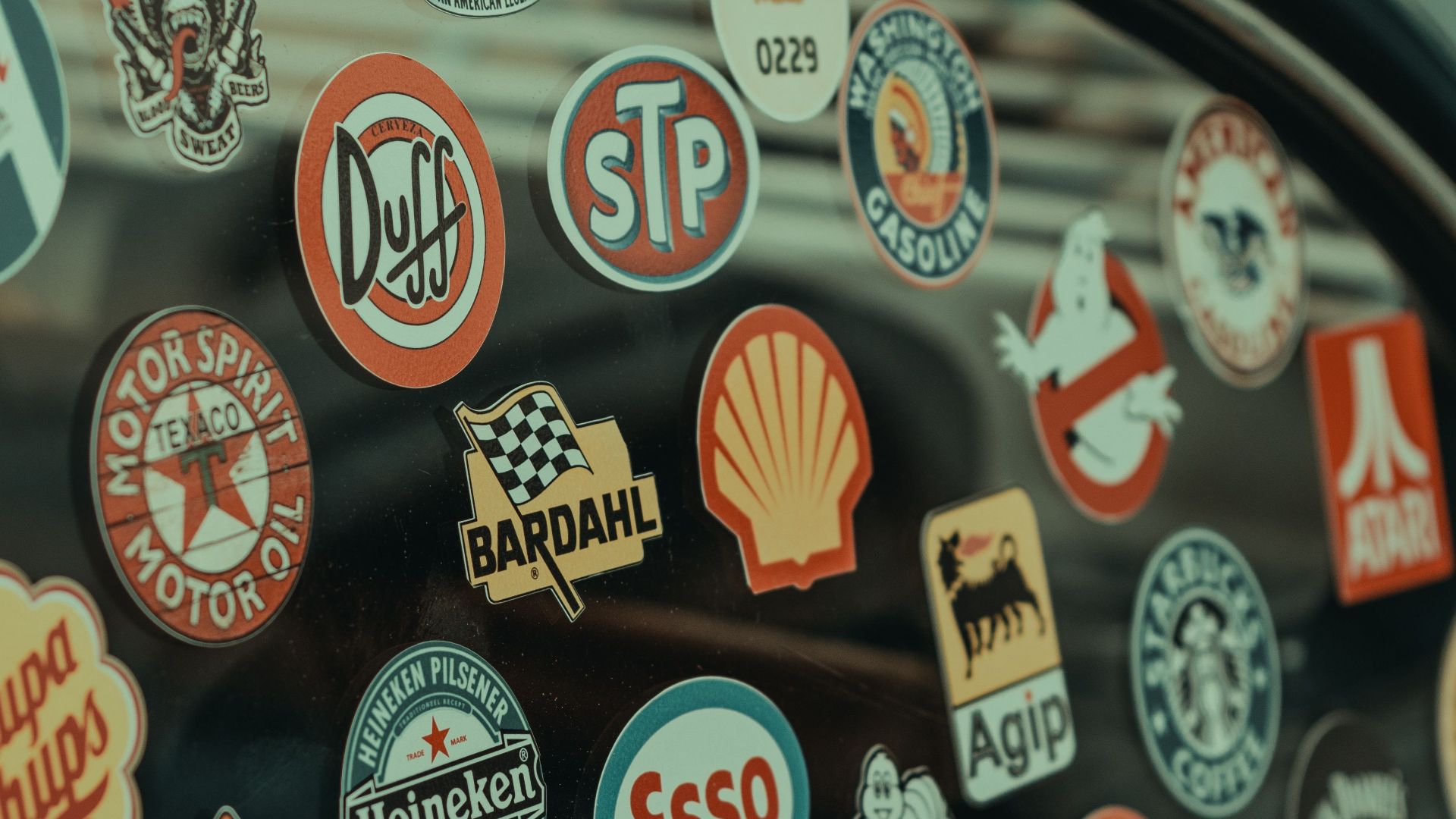 Close-up of a car window adorned with vintage logo stickers, including iconic brands.