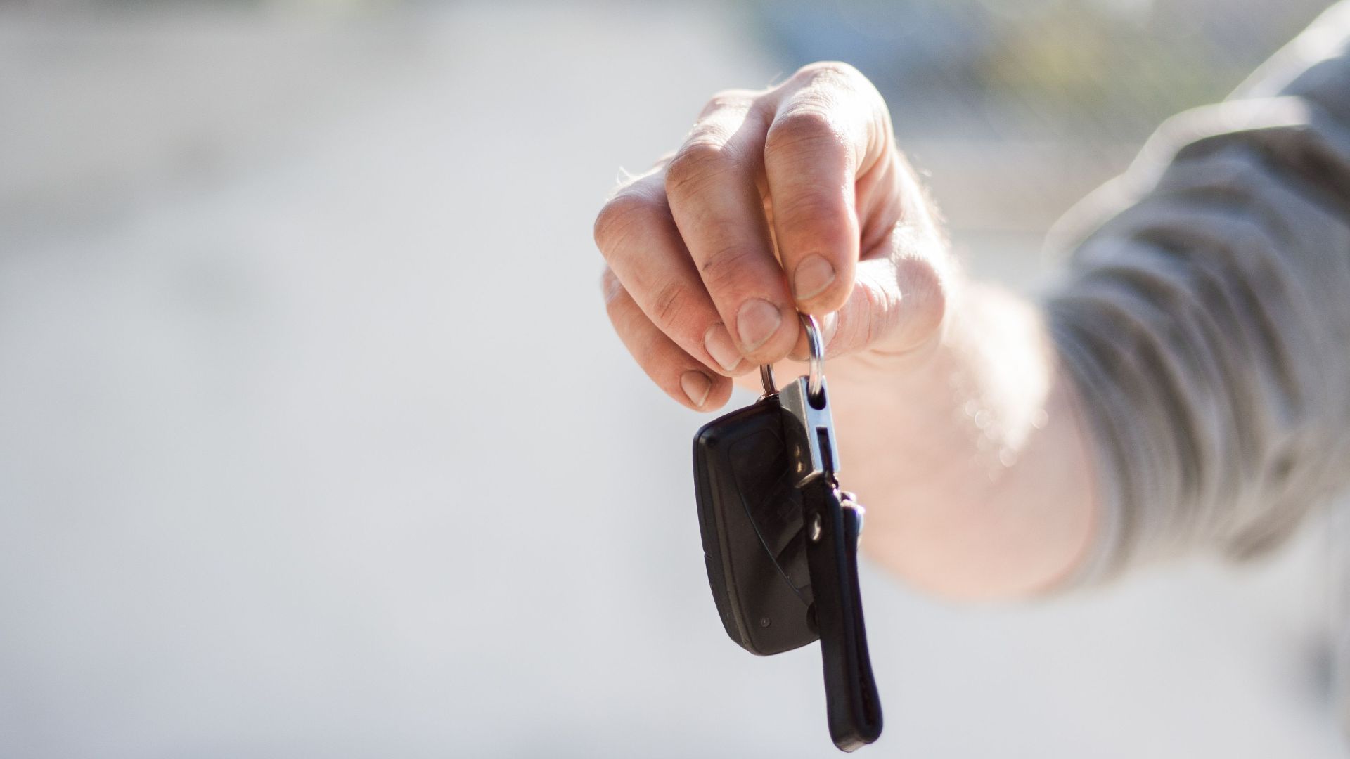 Close-up of a hand handing over car keys, signifying purchase or rental.