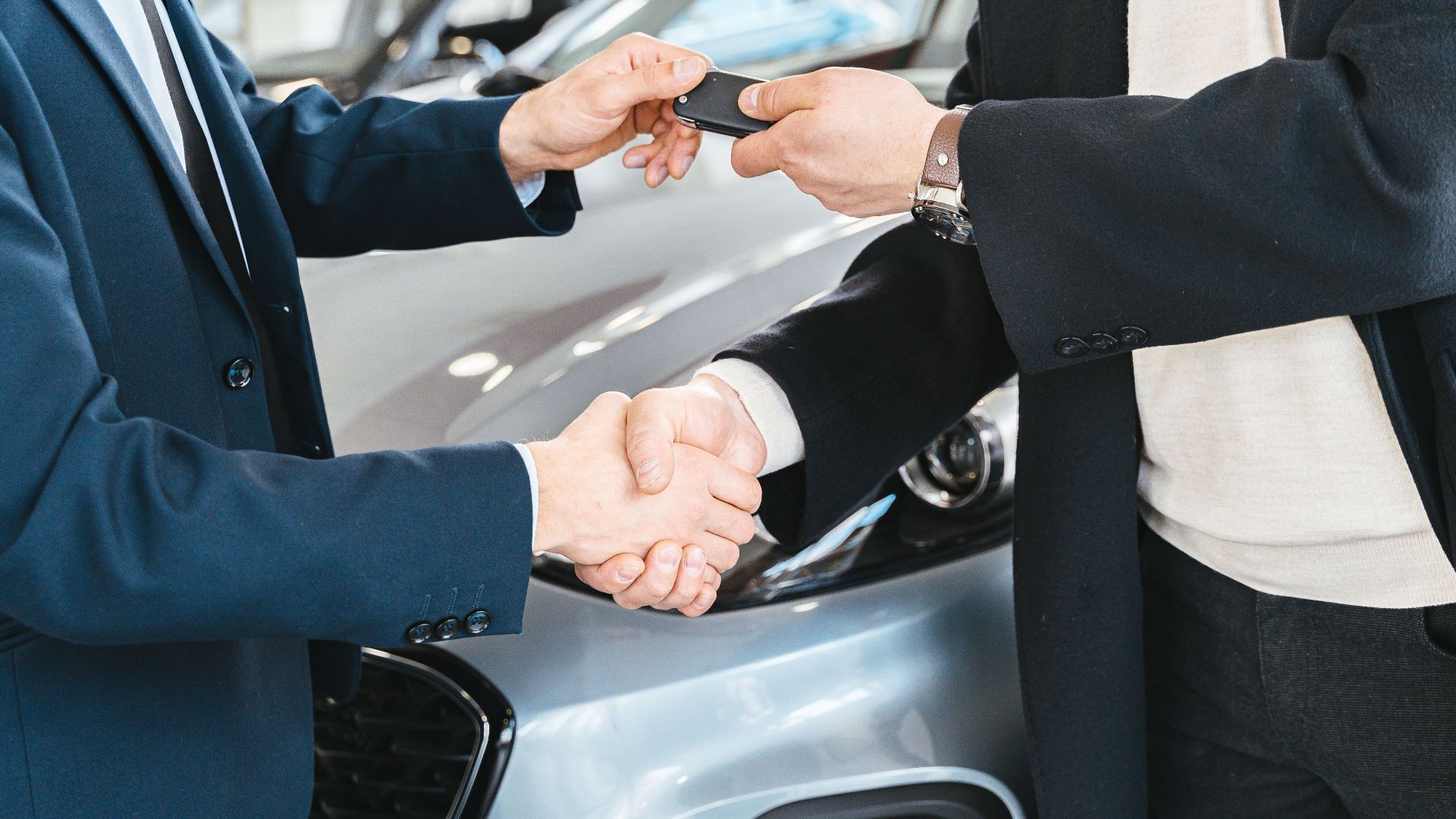 Two businessmen shaking hands and exchanging car keys in a dealership. Symbolizes a successful deal.