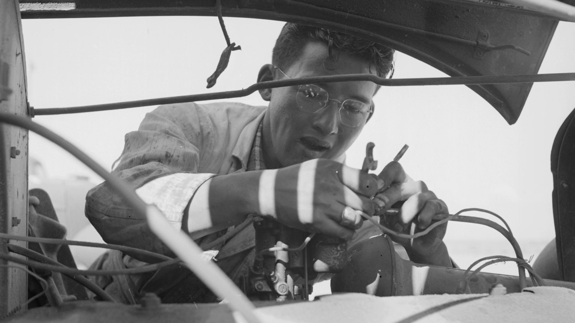 Scope and content: The full caption for this photograph reads: Topaz, Utah. A young resident at the Topaz Relocation Center adjusting a carburetor on a well worn War Relocation Authority truck.