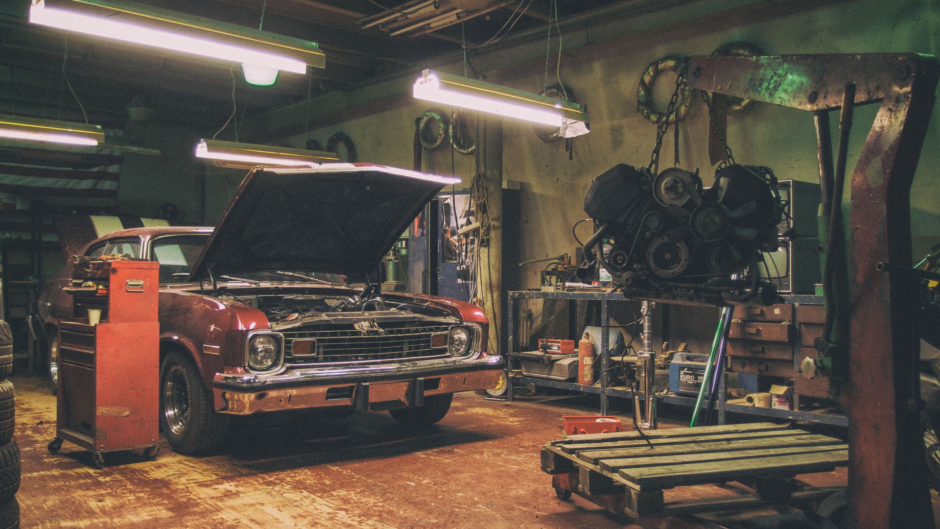 Vintage interior of a car repair shop with an old red American car and car engine on the crane. The automobile is ready for an engine replacement. Photographed by Martin Vorel - https://martinvorel.com