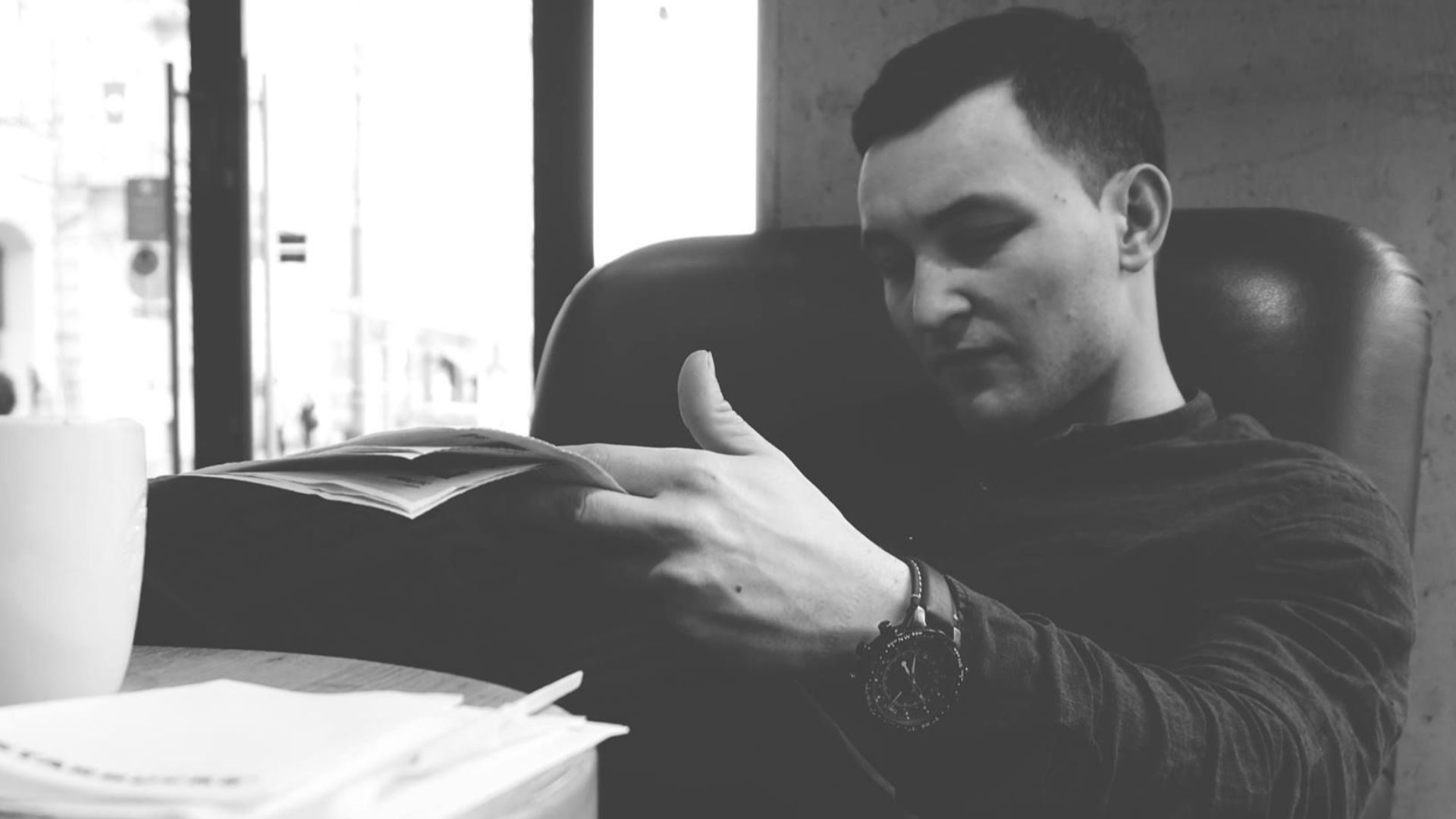 A man sits comfortably in a cafe chair reading a newspaper. Monochrome style.