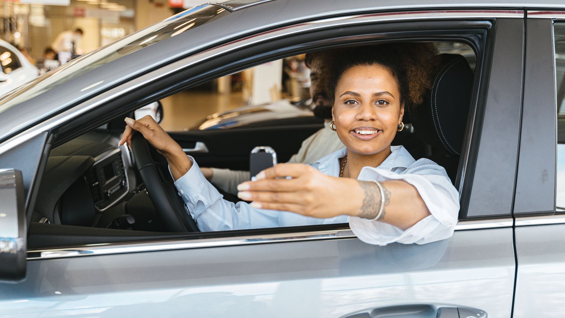 Smiling woman sitting in her new car holding keys, celebrating purchase.