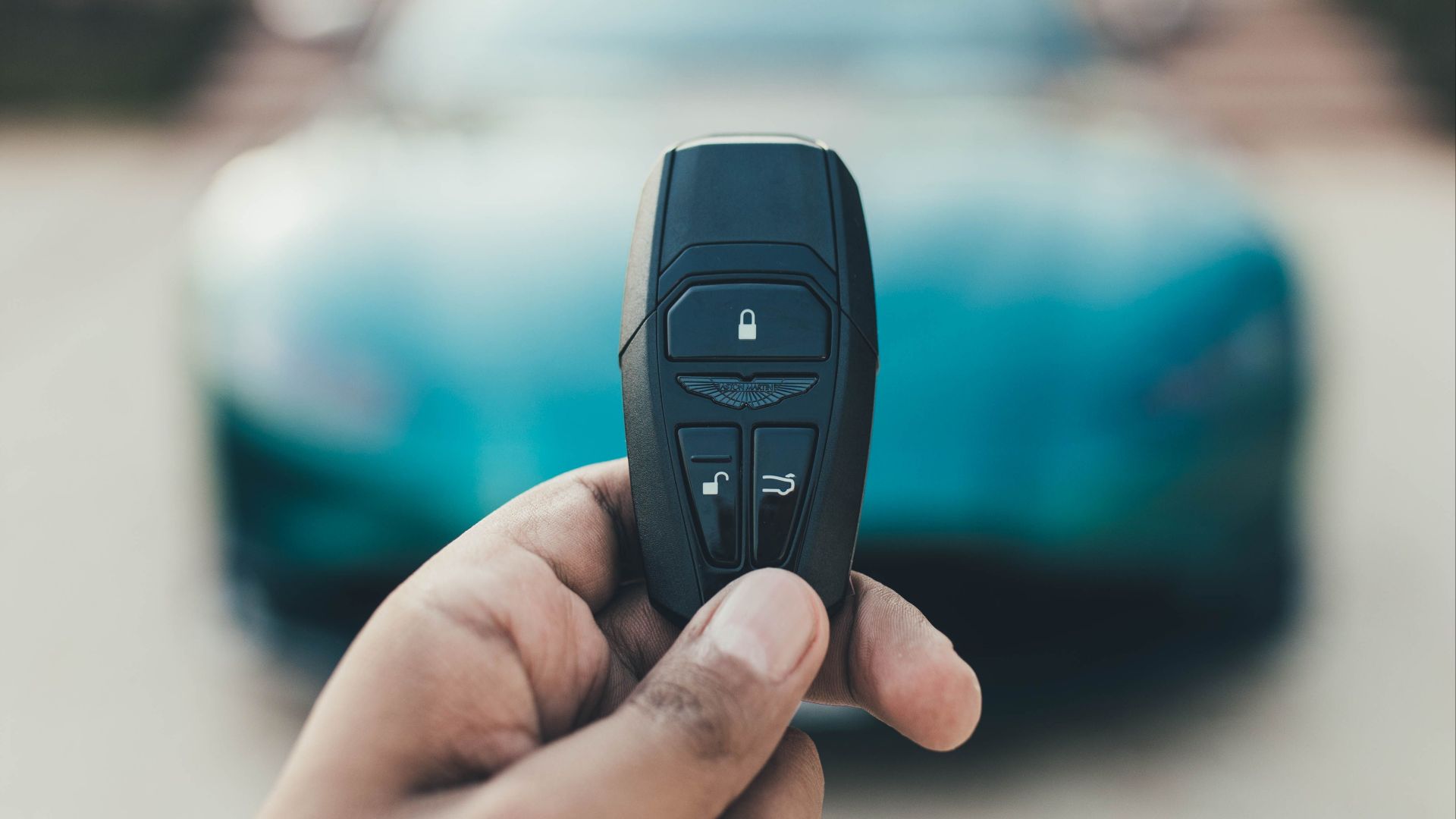 A close-up view of a hand holding a luxury car key with a blurred car in the background. Captured in New Delhi, India.