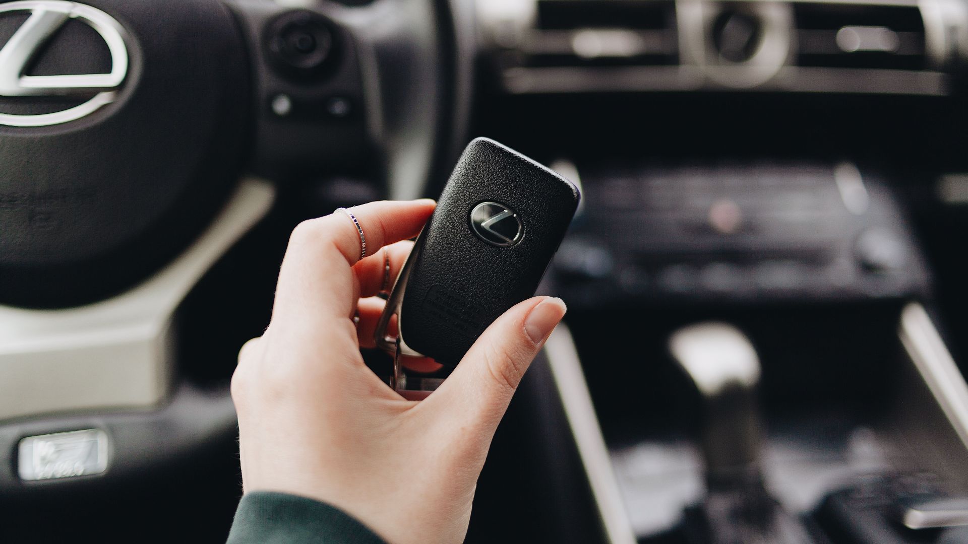 Person holding a Lexus car key inside a luxury vehicle's interior, showcasing brand elegance.