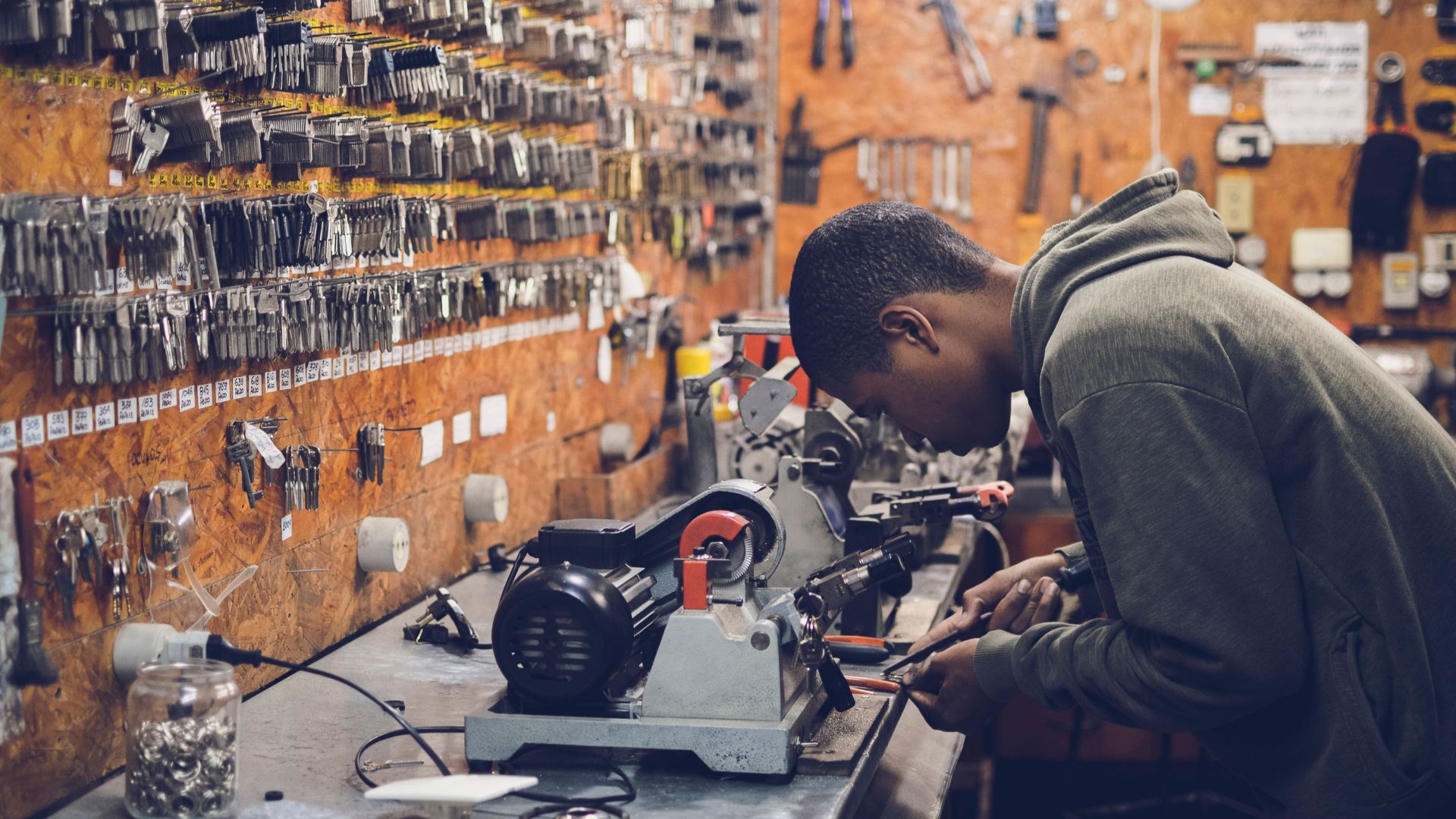 A focused craftsman works in a key-making workshop surrounded by tools and equipment.