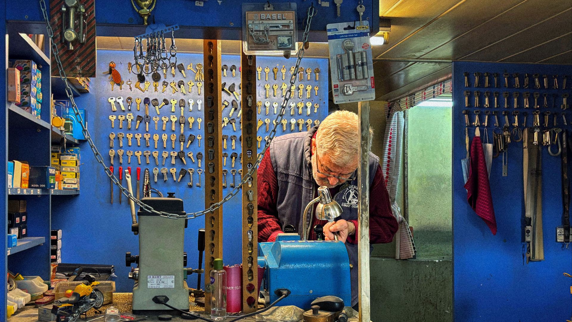 A senior locksmith crafts a key in his hardware shop filled with locks and keys.