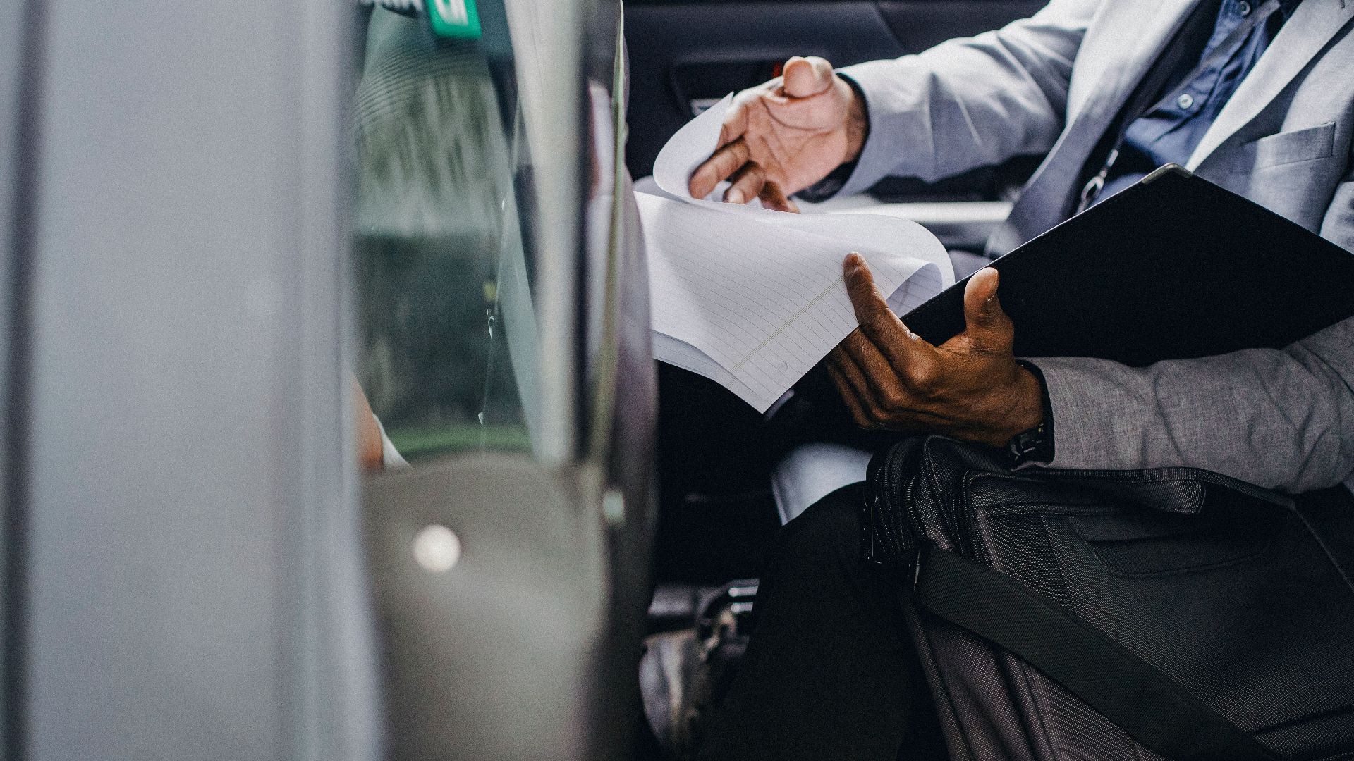 Busy crop anonymous African American male preparing important papers in folder while sitting in automobile