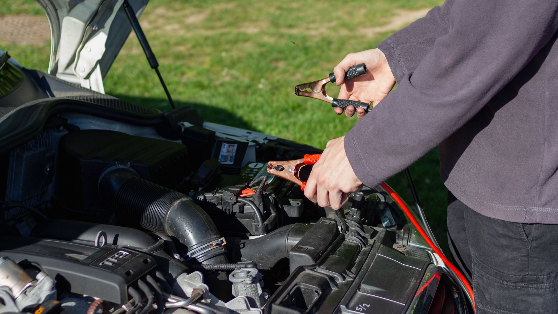 Close-up of mechanic using jumper cables to jump-start a car battery outdoors.
