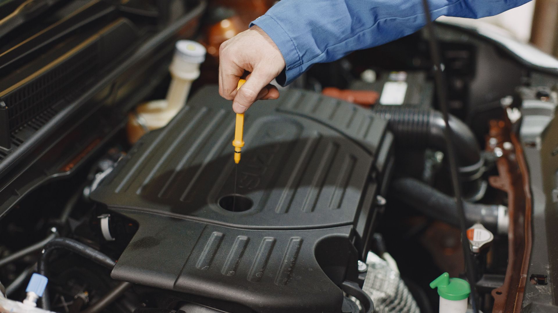 Close-up of a person checking engine oil using a dipstick in a car's engine bay.