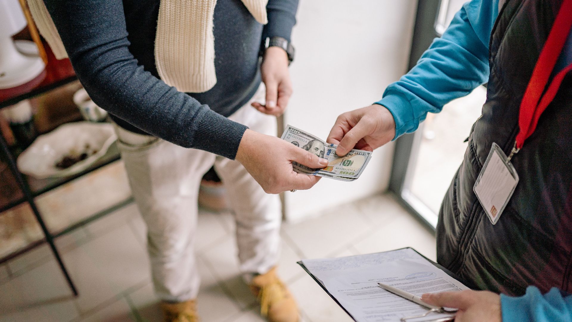 Close-up of hands exchanging cash during a transaction indoors, highlighting payment details.