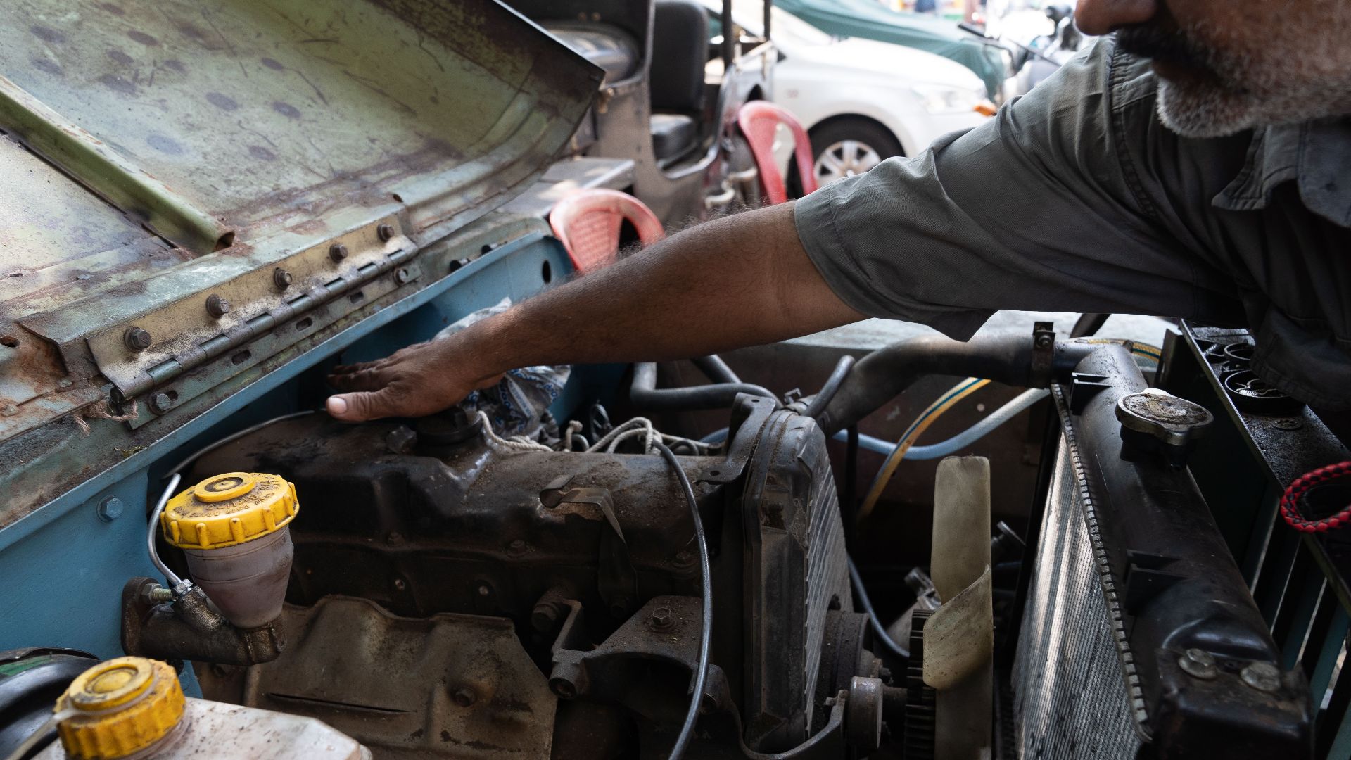 A mechanic tuning a jeep engine in an outdoor setting, highlighting vehicle maintenance.