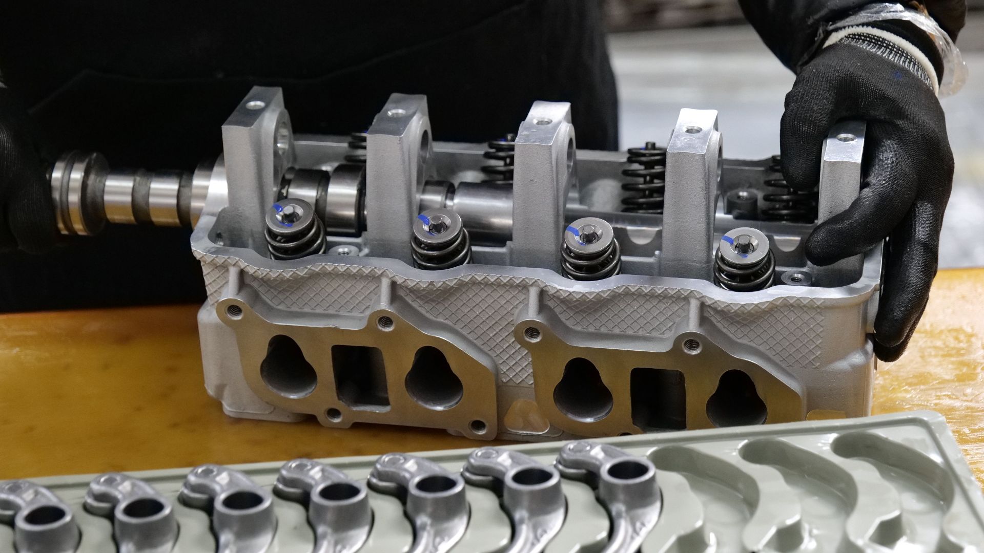 Mechanic assembling an engine cylinder head with precision components on a workbench.