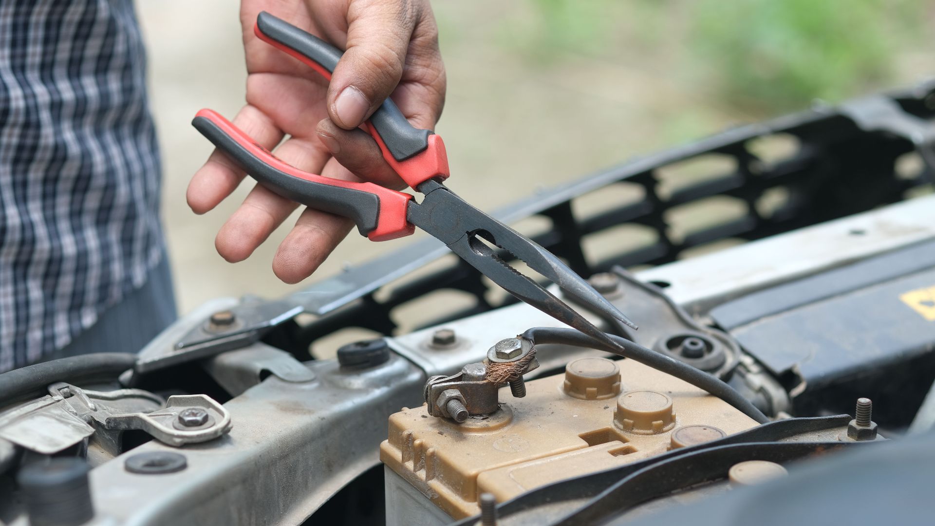 Person using pliers to check a car battery in an outdoor setting.