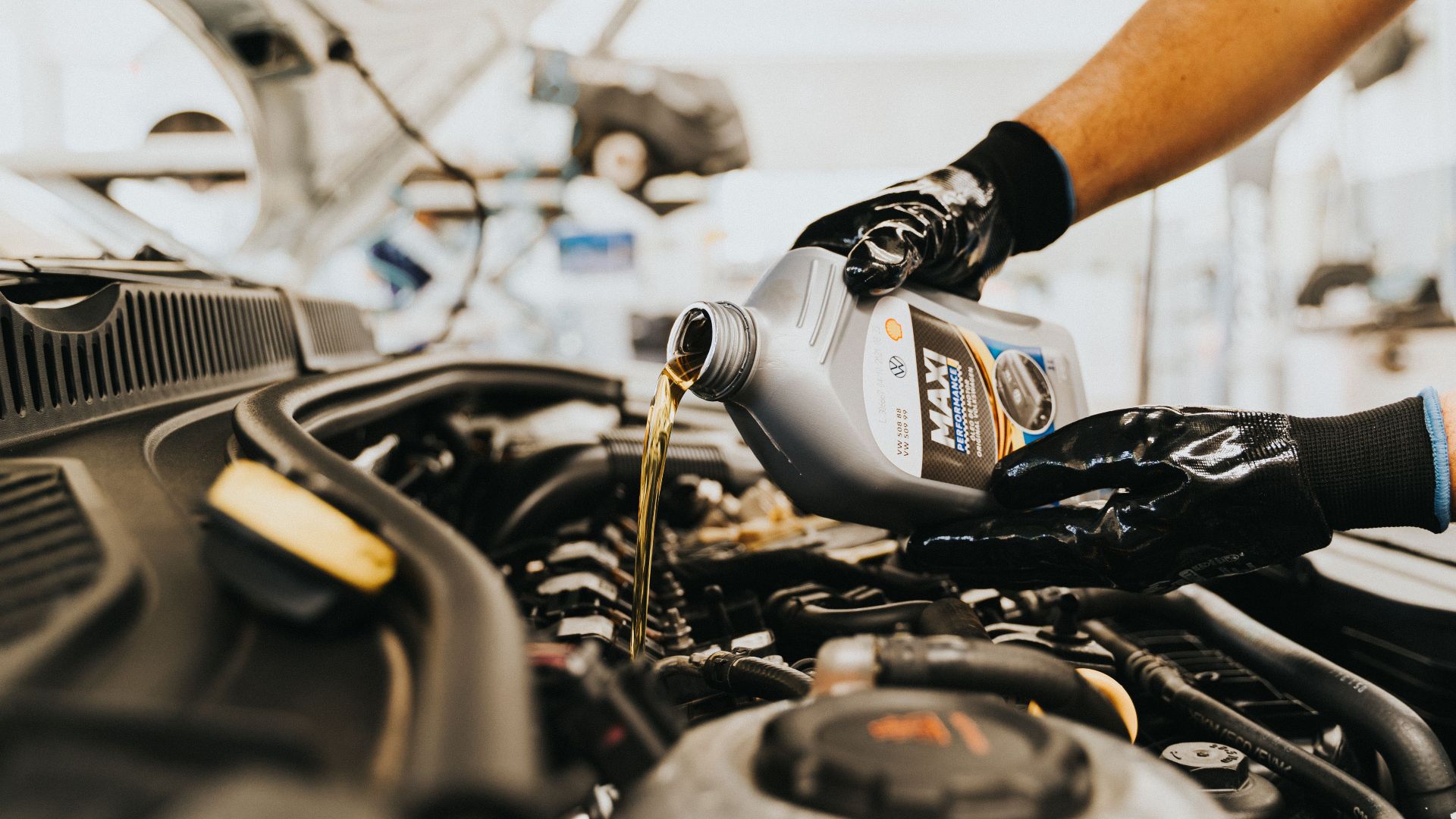 Close-up of a mechanic pouring engine oil into a car engine in an auto repair shop.