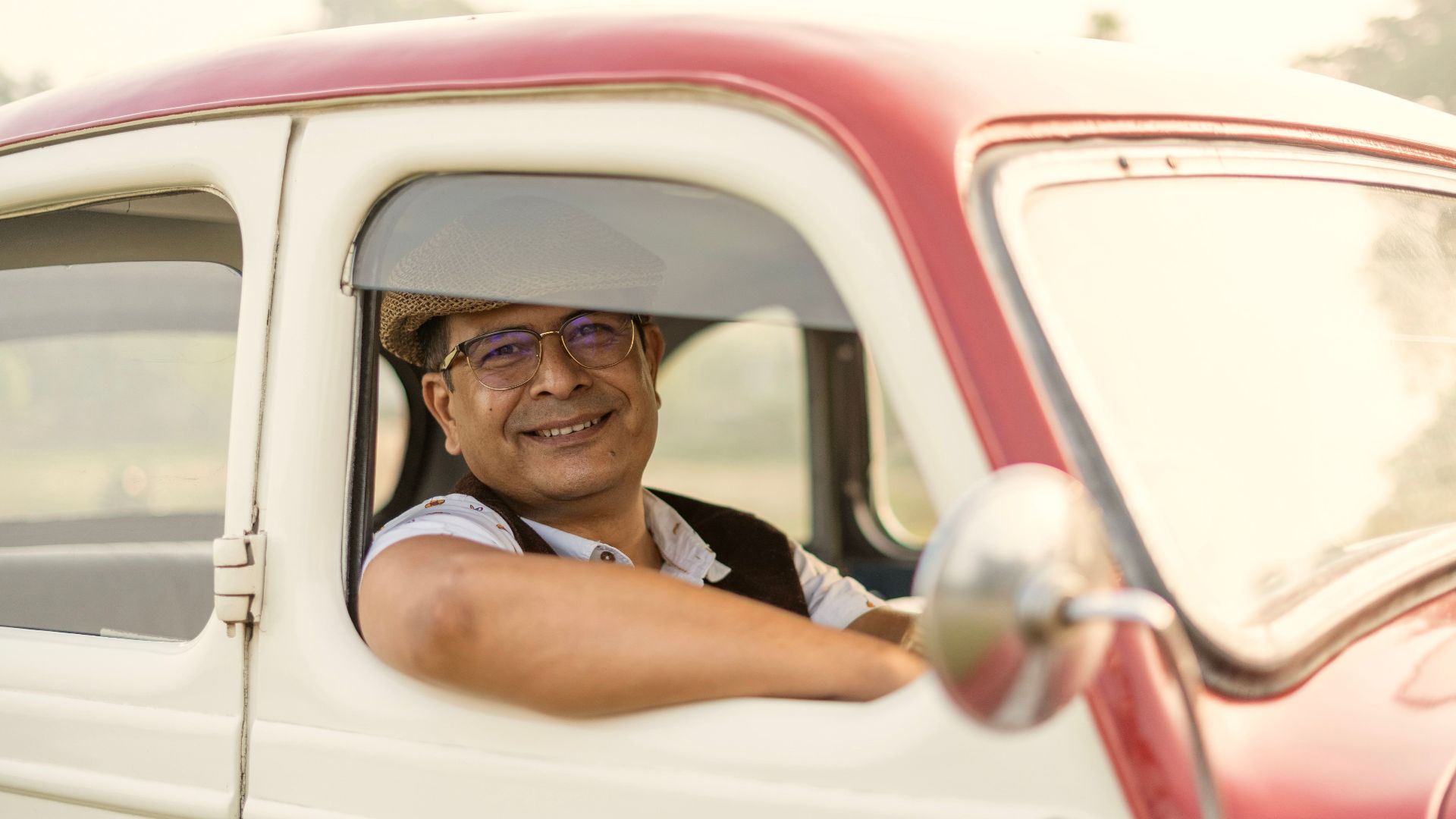 Cheerful man wearing a hat, enjoying a drive in a classic car.
