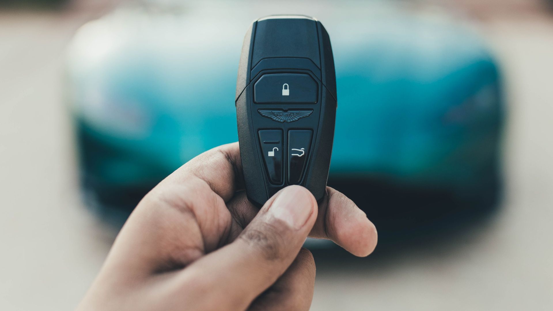 A close-up view of a hand holding a luxury car key with a blurred car in the background. Captured in New Delhi, India.