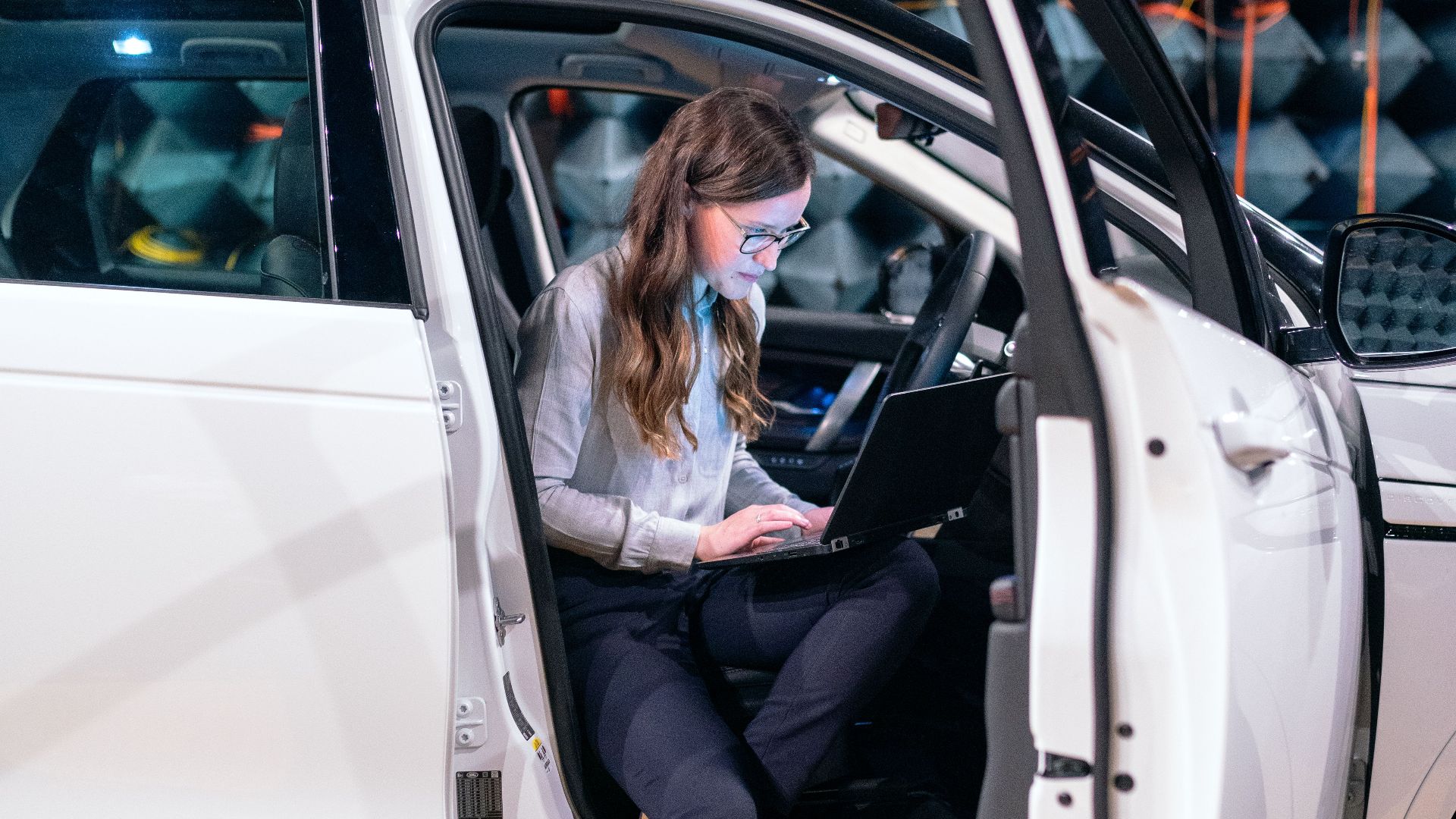 Sound engineer working on a laptop inside a car for acoustic testing in an anechoic chamber.