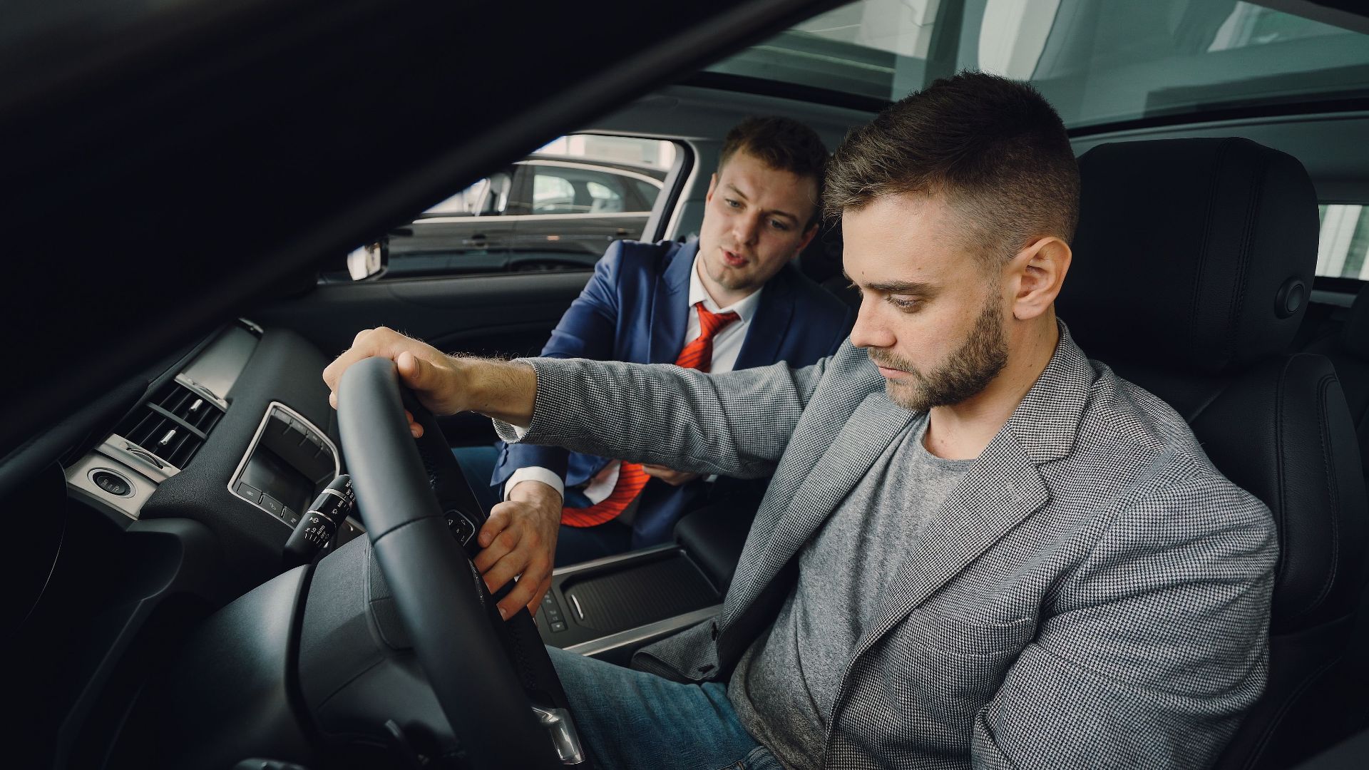 Salesman demonstrating car features to potential buyer inside vehicle showroom.