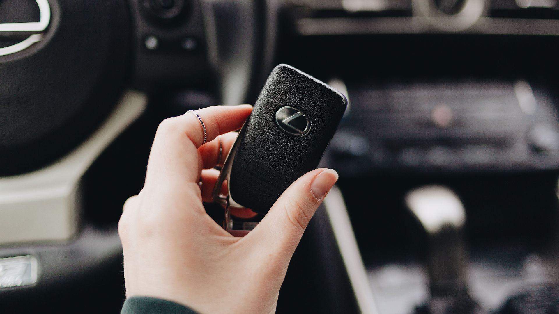 Person holding a Lexus car key inside a luxury vehicle's interior, showcasing brand elegance.