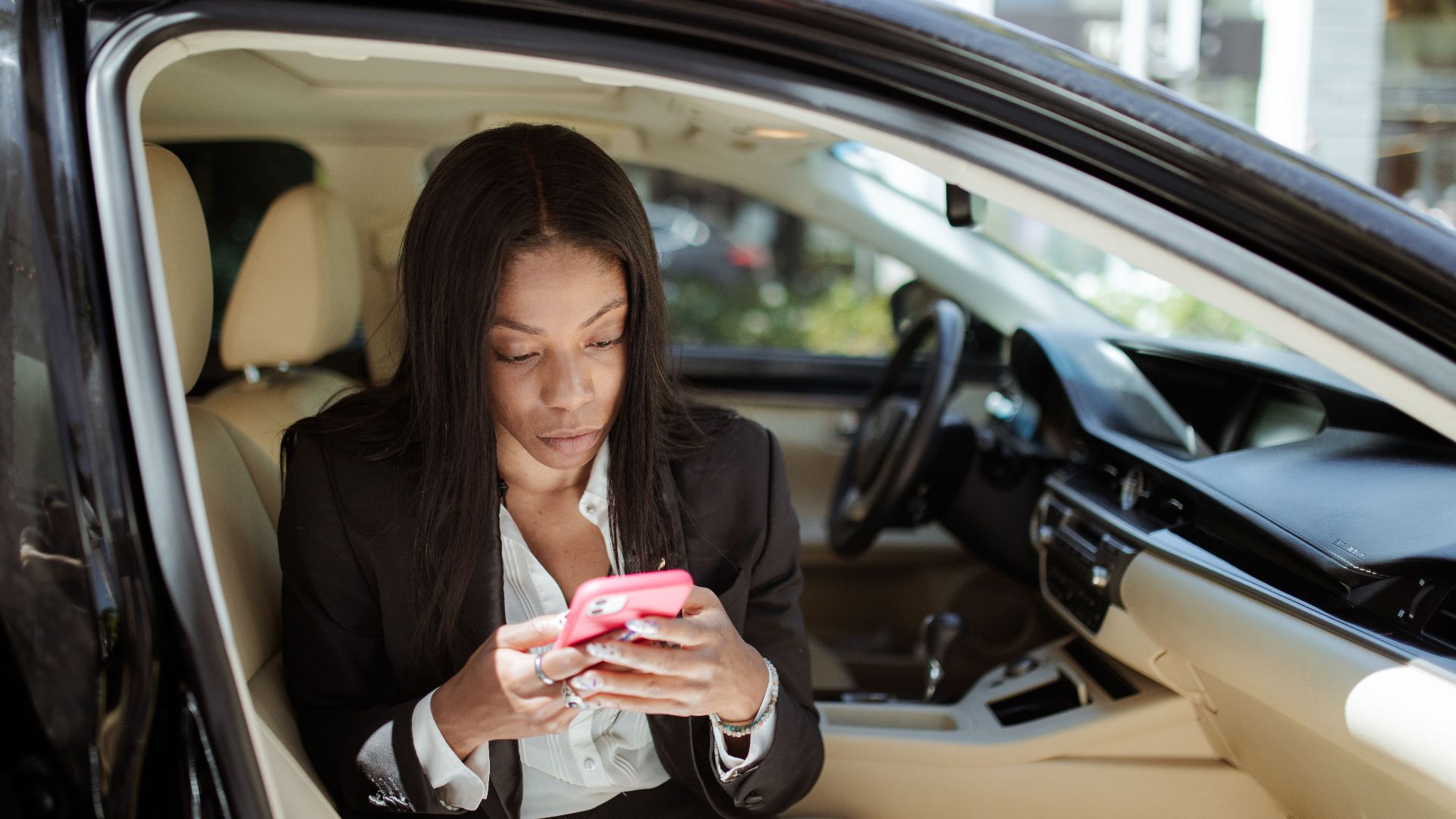 A businesswoman uses her smartphone while seated in a car, focusing intently on the screen.