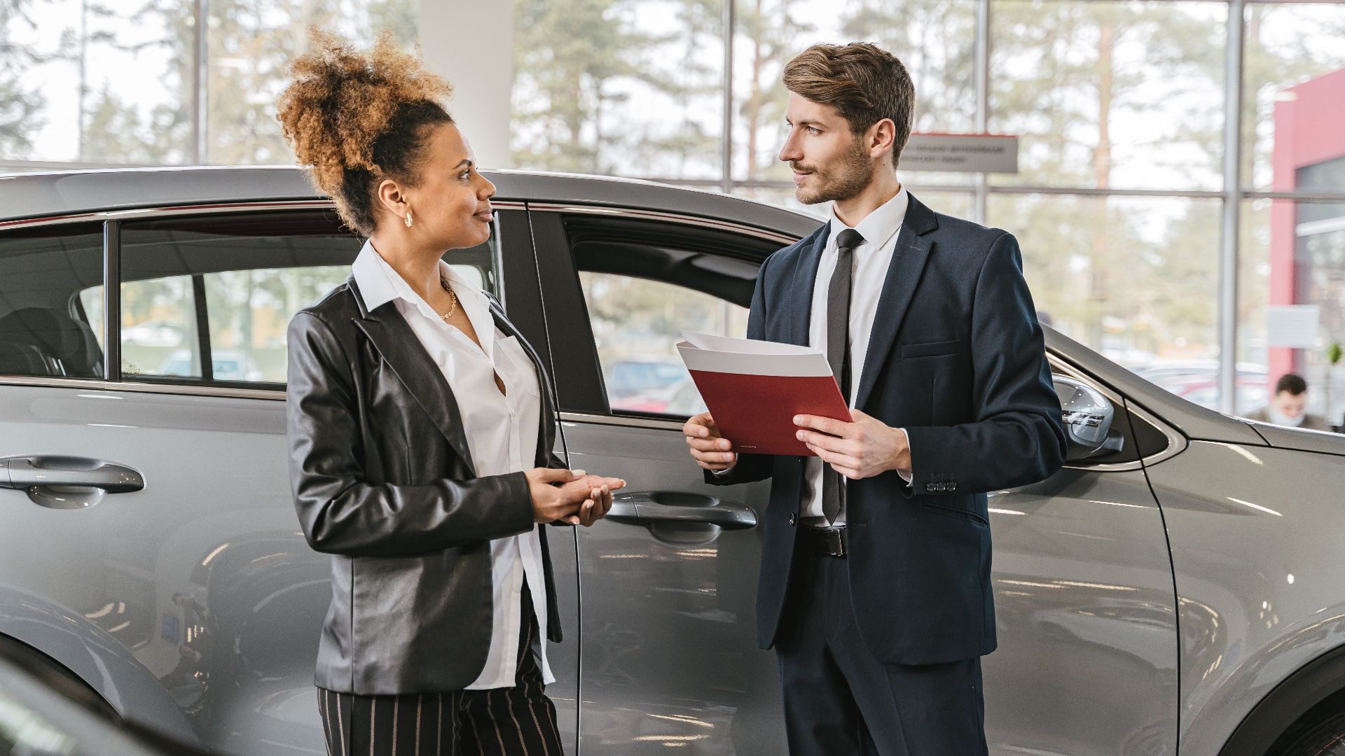 A woman discussing car purchase with a dealer inside a car dealership showroom.