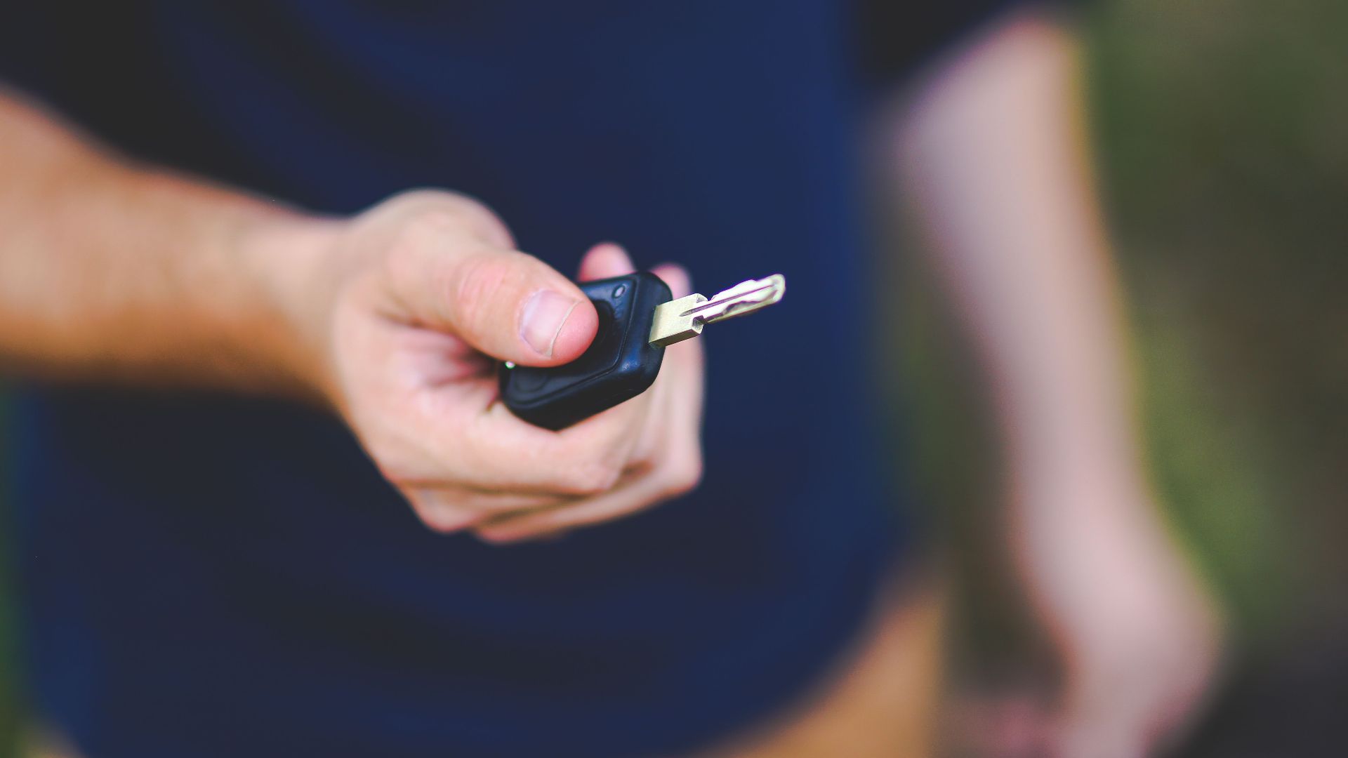 A hand holding a car key outdoors, emphasizing security and control.