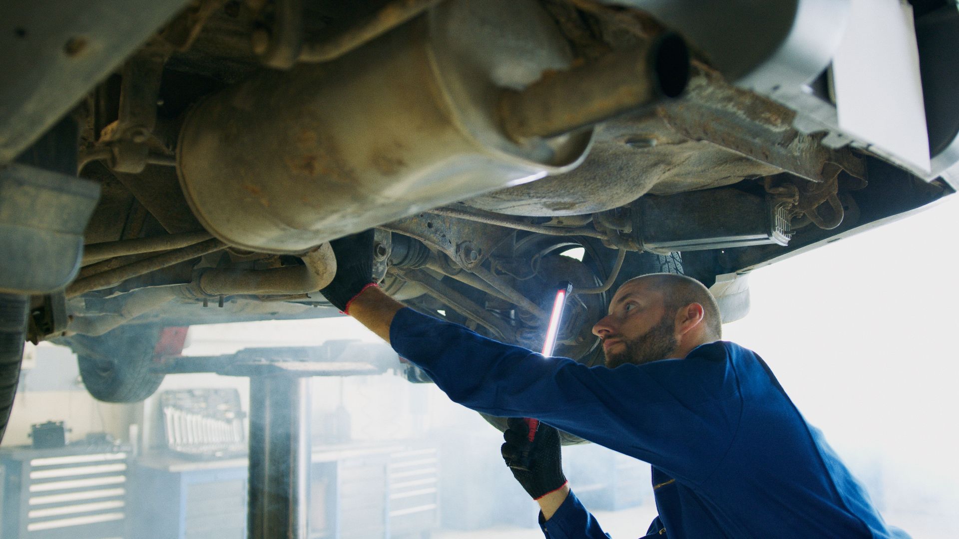 Skilled mechanic performing thorough maintenance under a vehicle in a professional garage setting.